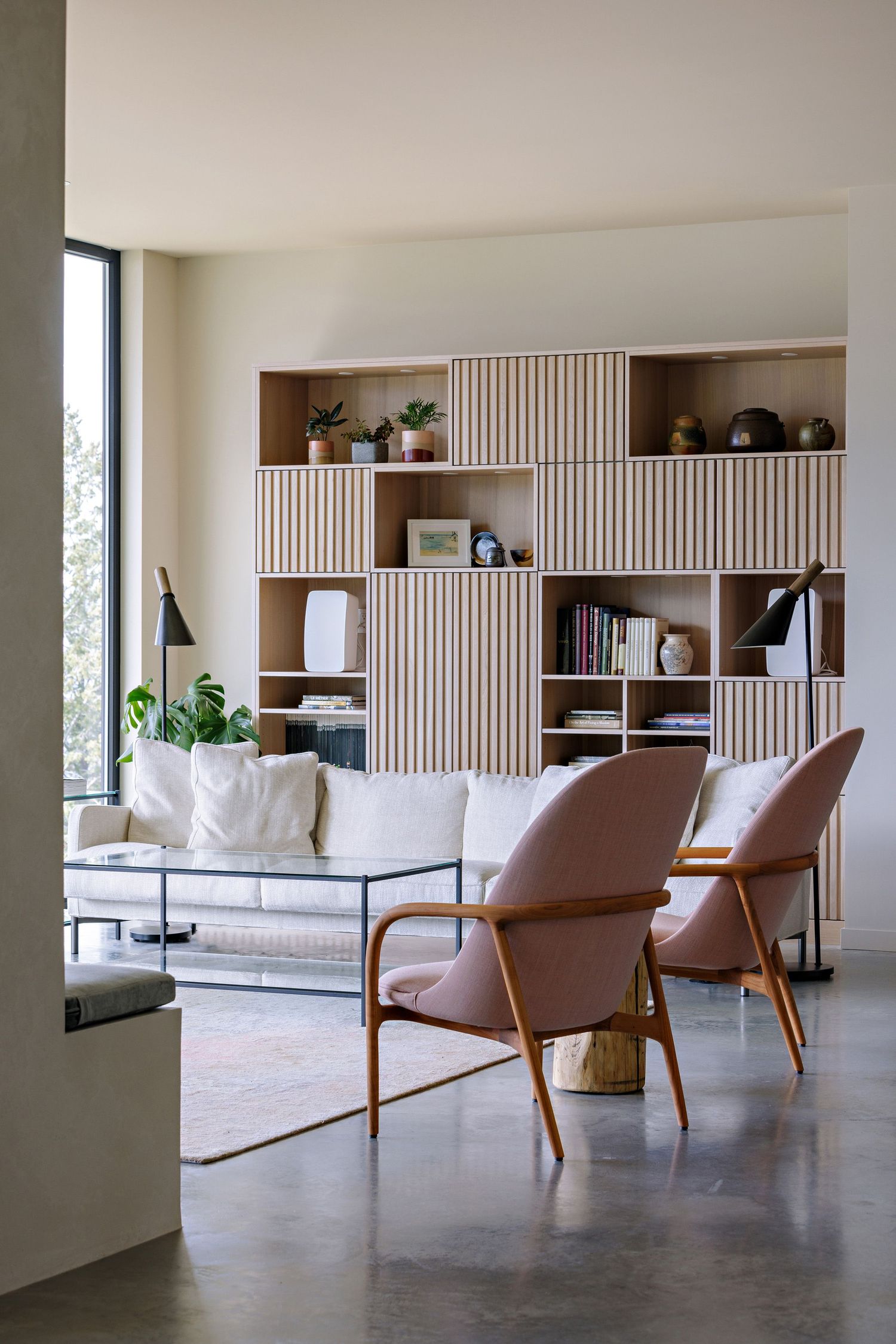 Modern living room with white sofa, brown chairs and built-in shelving featuring vertical wood slat panels.