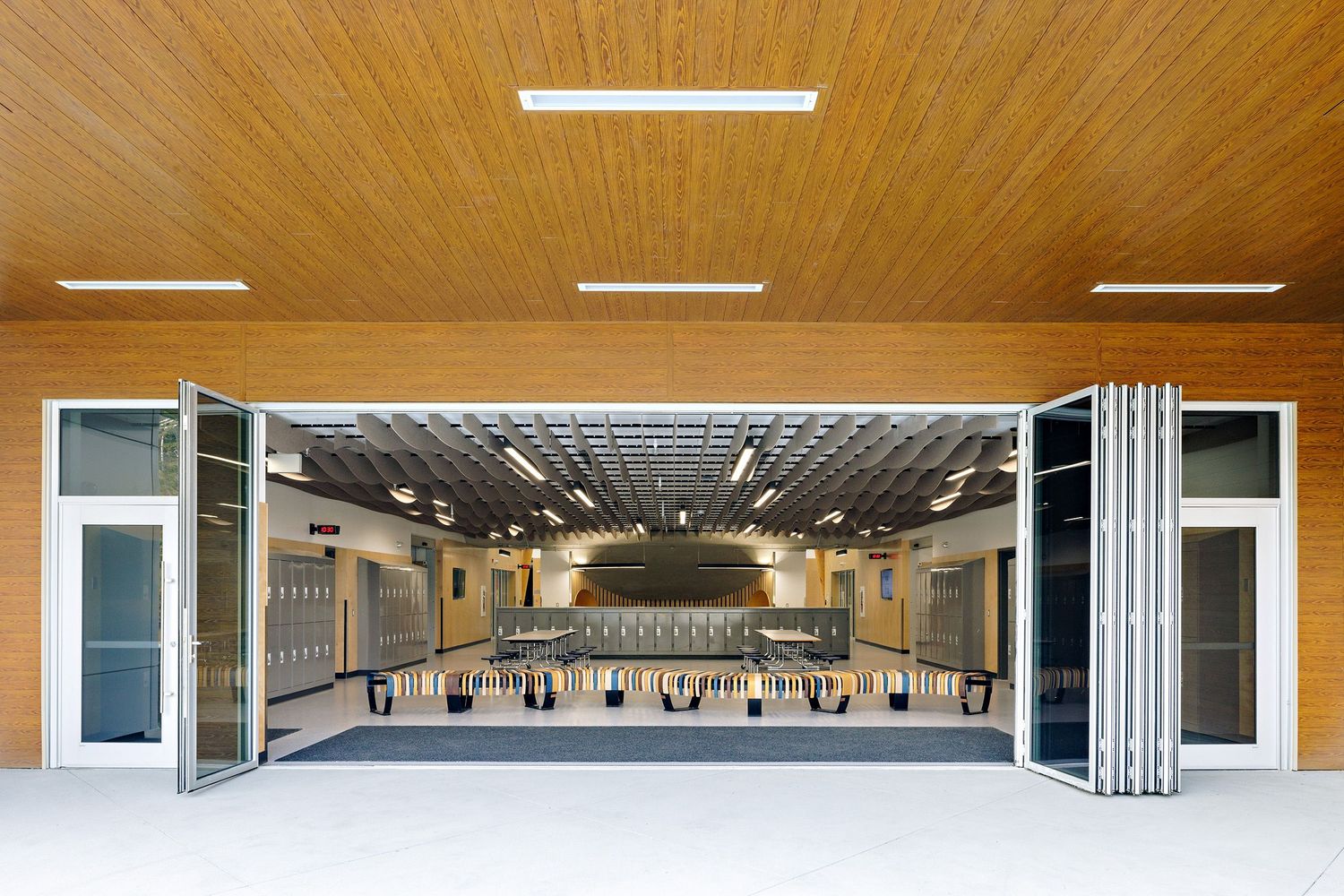 Large multi-purpose school auditorium or gymnasium with folding doors and wood-paneled ceiling.