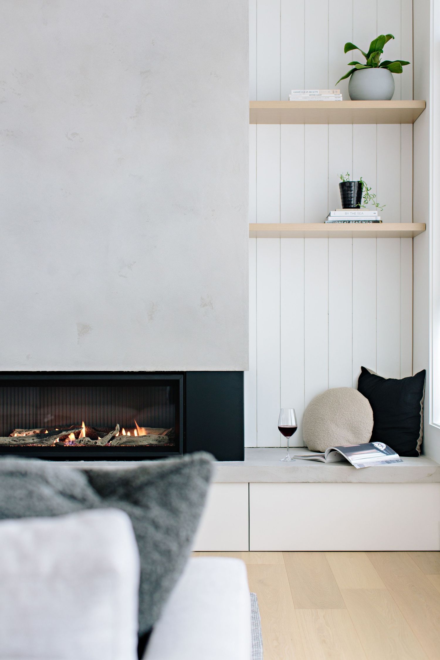 Modern living room with sleek gas fireplace, floating wood shelves, and cozy seating area with wine glass.