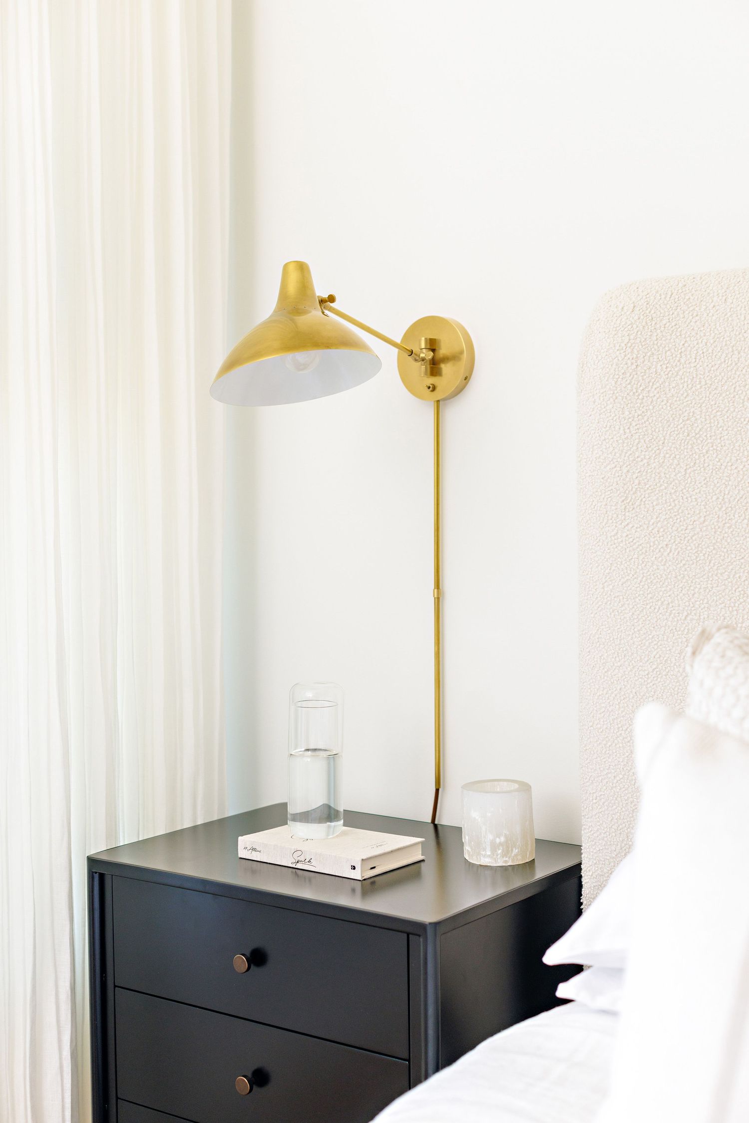Minimalist bedside table with brass wall sconce and decorative accessories.