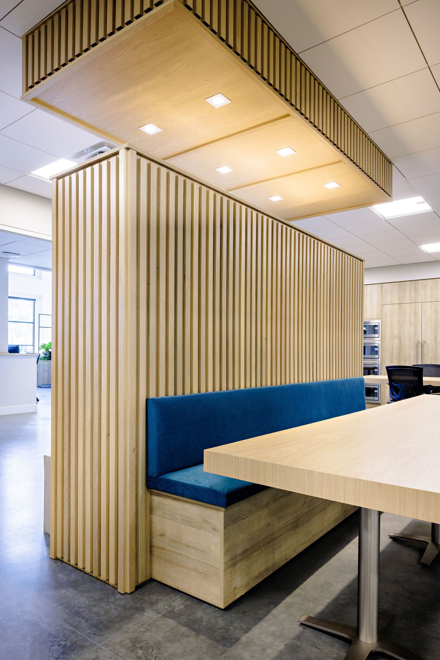 Contemporary office booth with vertical wood slats, blue upholstered seating, and built-in lighting.