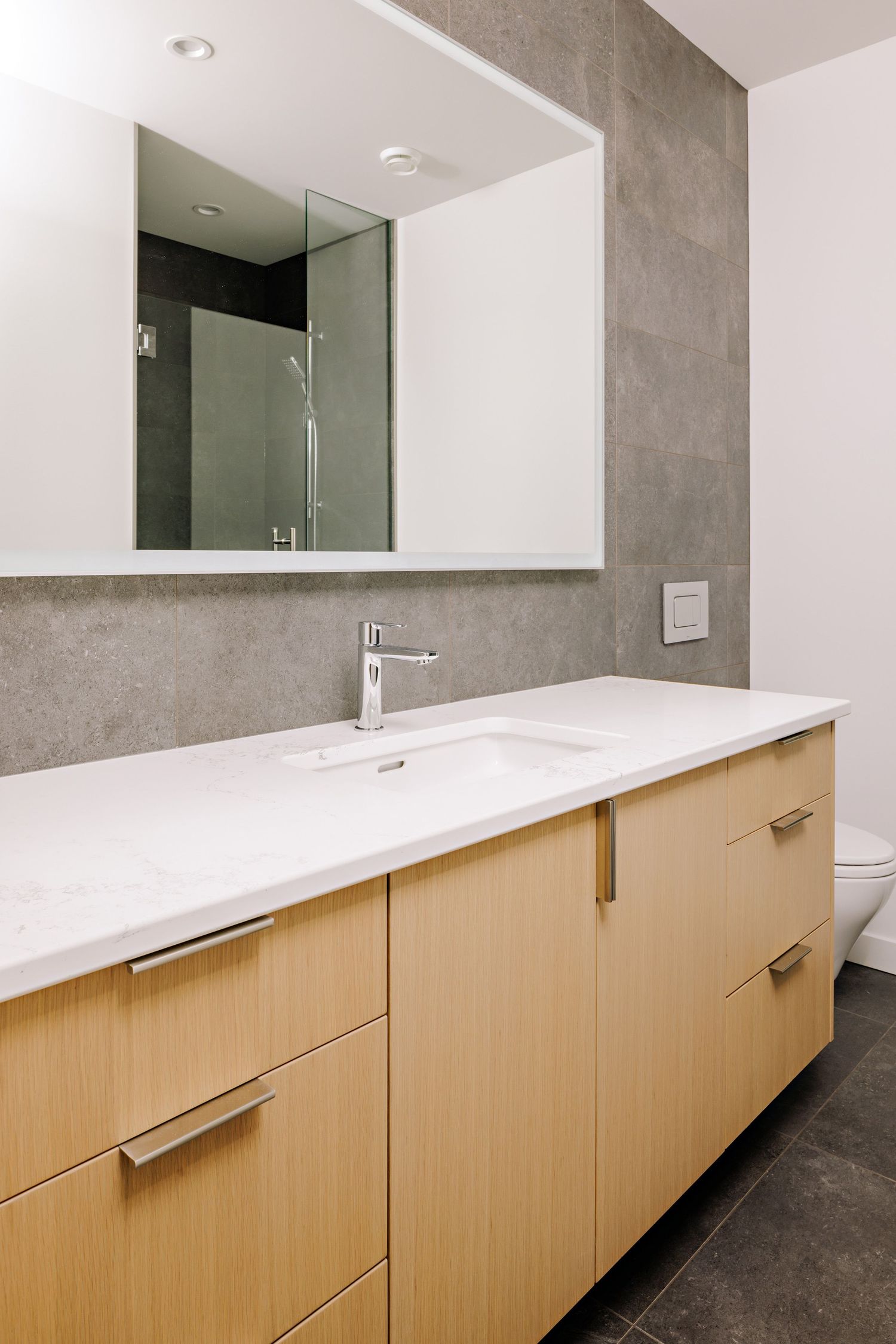 Modern bathroom interior with light wood vanity, white countertop, and large frameless mirror.