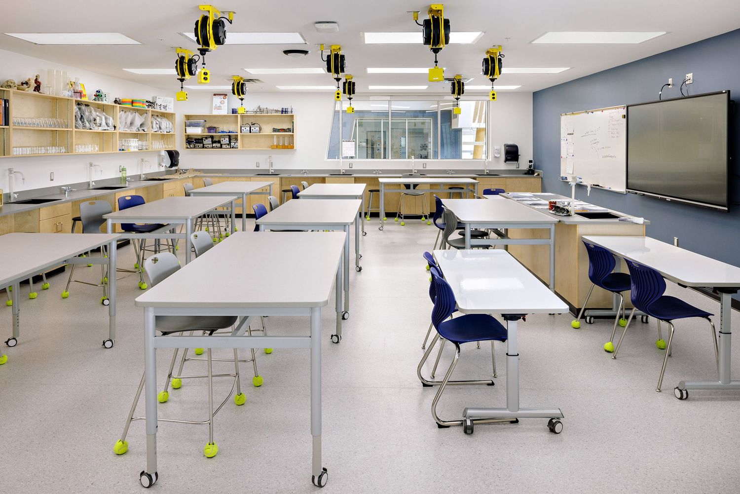 Modern science classroom with white lab tables, blue chairs, and decorative bee pendant lamps hanging from the ceiling.
