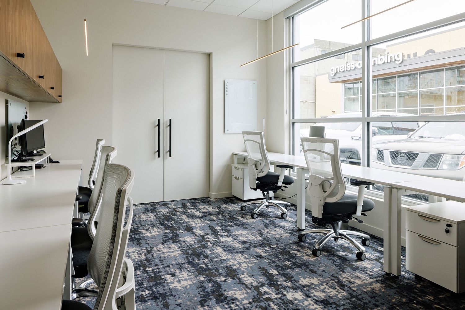 Modern office space with white furniture, patterned blue carpeting, and large windows providing natural light.
