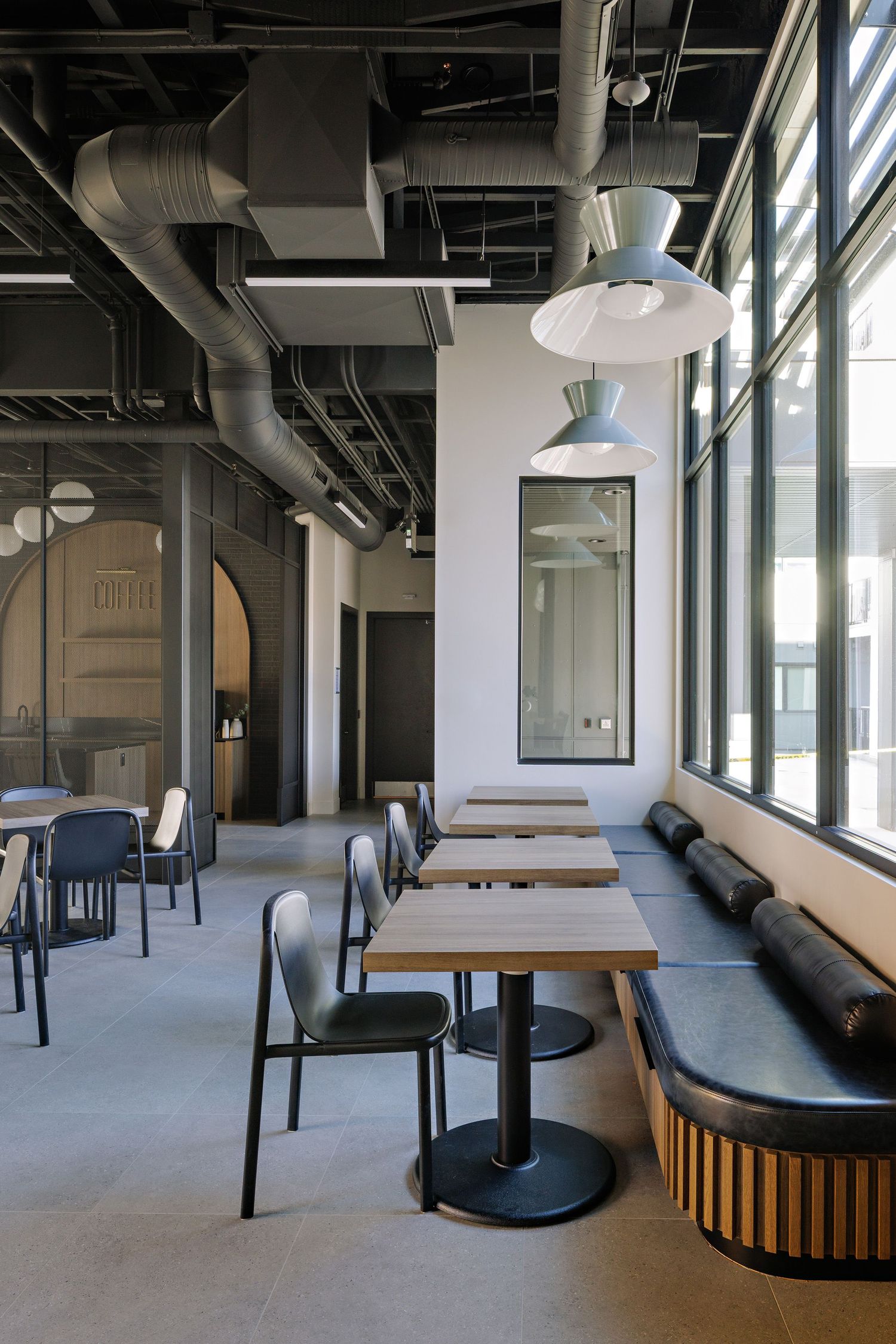 Modern industrial office space with exposed ceiling, large windows, and round booth seating arrangements in an open layout.
