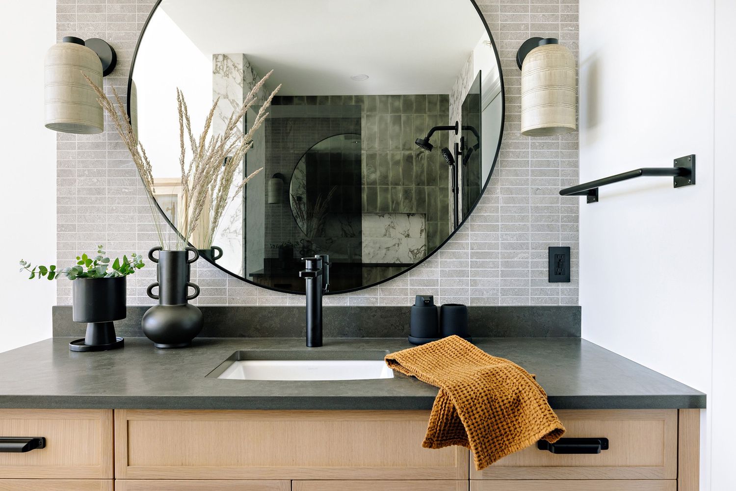 Contemporary bathroom vanity with round mirror, dark countertop, and warm accents.