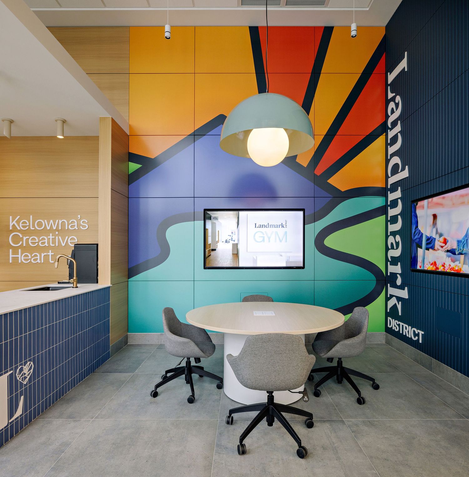 Contemporary meeting space with round table, black chairs and vibrant wall art featuring yellow and blue geometric design.
