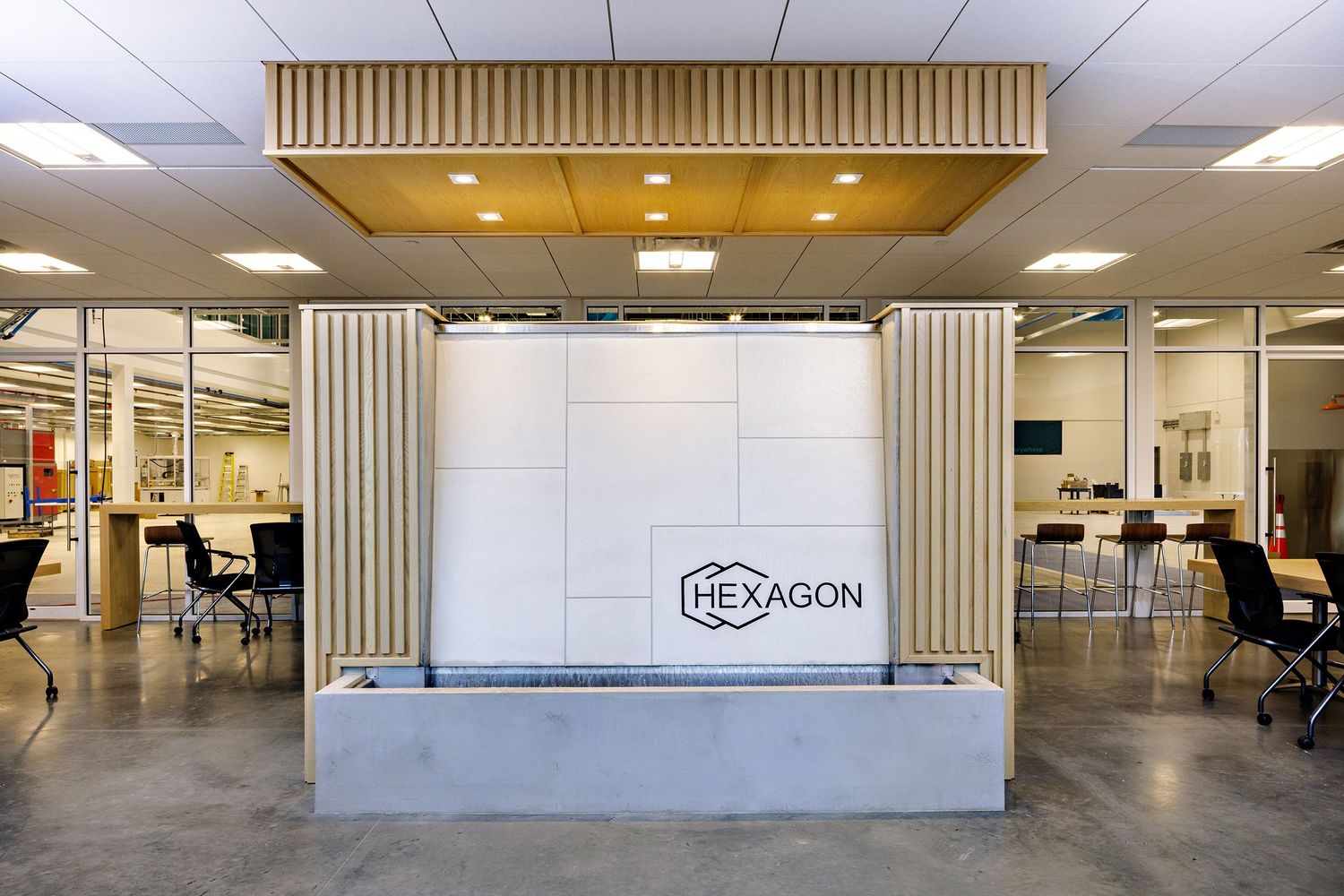 Modern office lobby featuring a sleek reception desk with wood accents and a gray concrete base under recessed lighting.