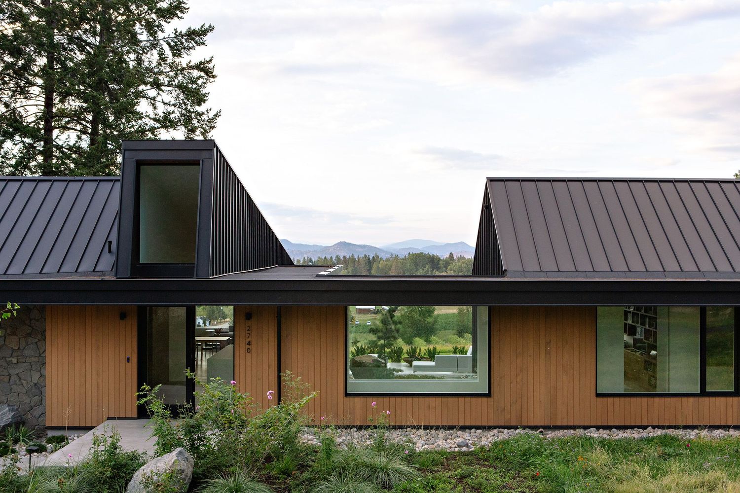 Modern house with cedar siding and black metal roof features angular design and mountain views through large windows.