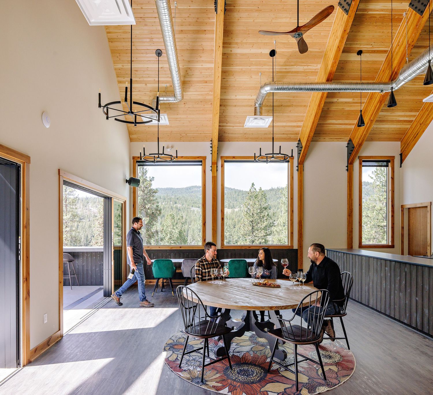 Modern office meeting space with wooden beams, large windows, and a round table situated on a patterned area rug.