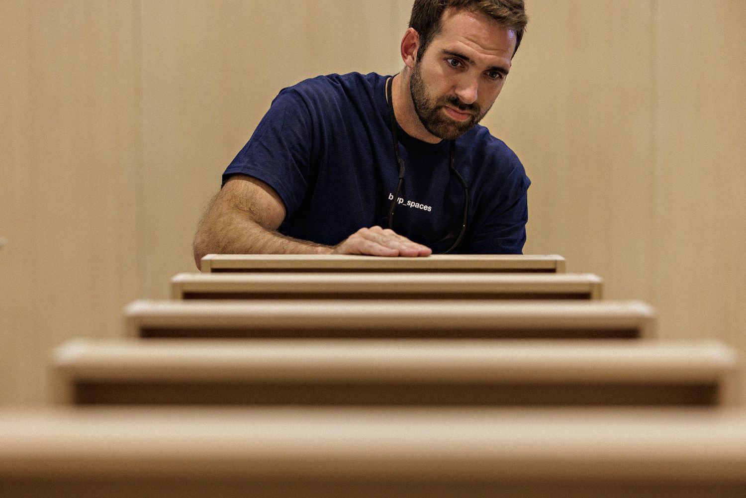Craftsman wearing a navy shirt carefully examines a wooden surface while working in a woodshop.