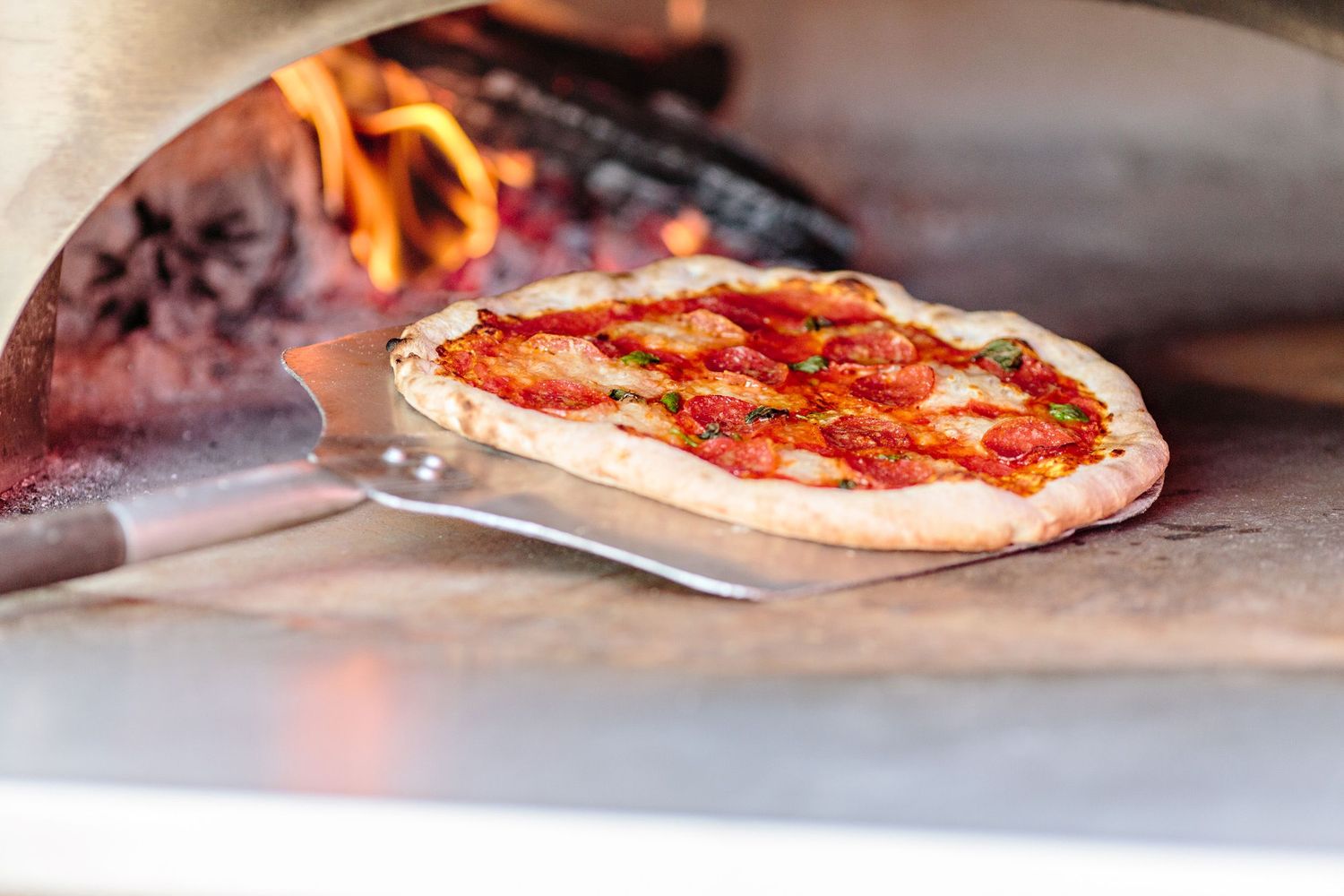 Wood-fired Margherita pizza with melted mozzarella and tomato sauce cooking in a traditional brick oven with visible flames.