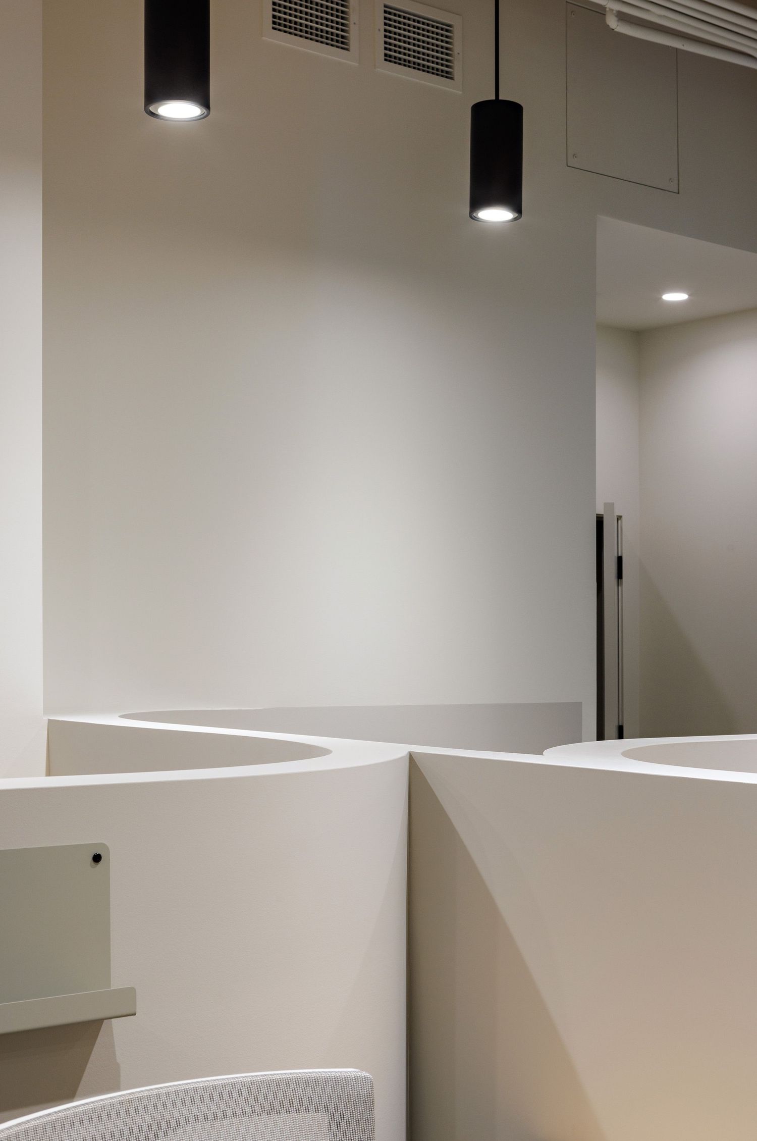 Modern office interior with white angular walls and black cylindrical pendant lights creating a minimalist geometric space.