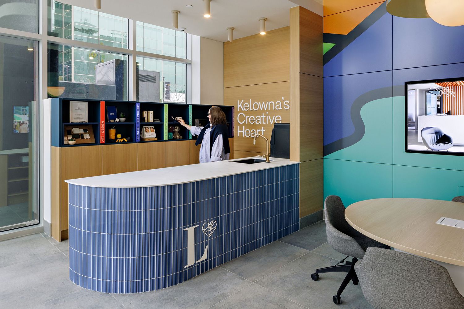 Modern office reception area with curved blue tile desk and colorful geometric wall mural in professional workspace.