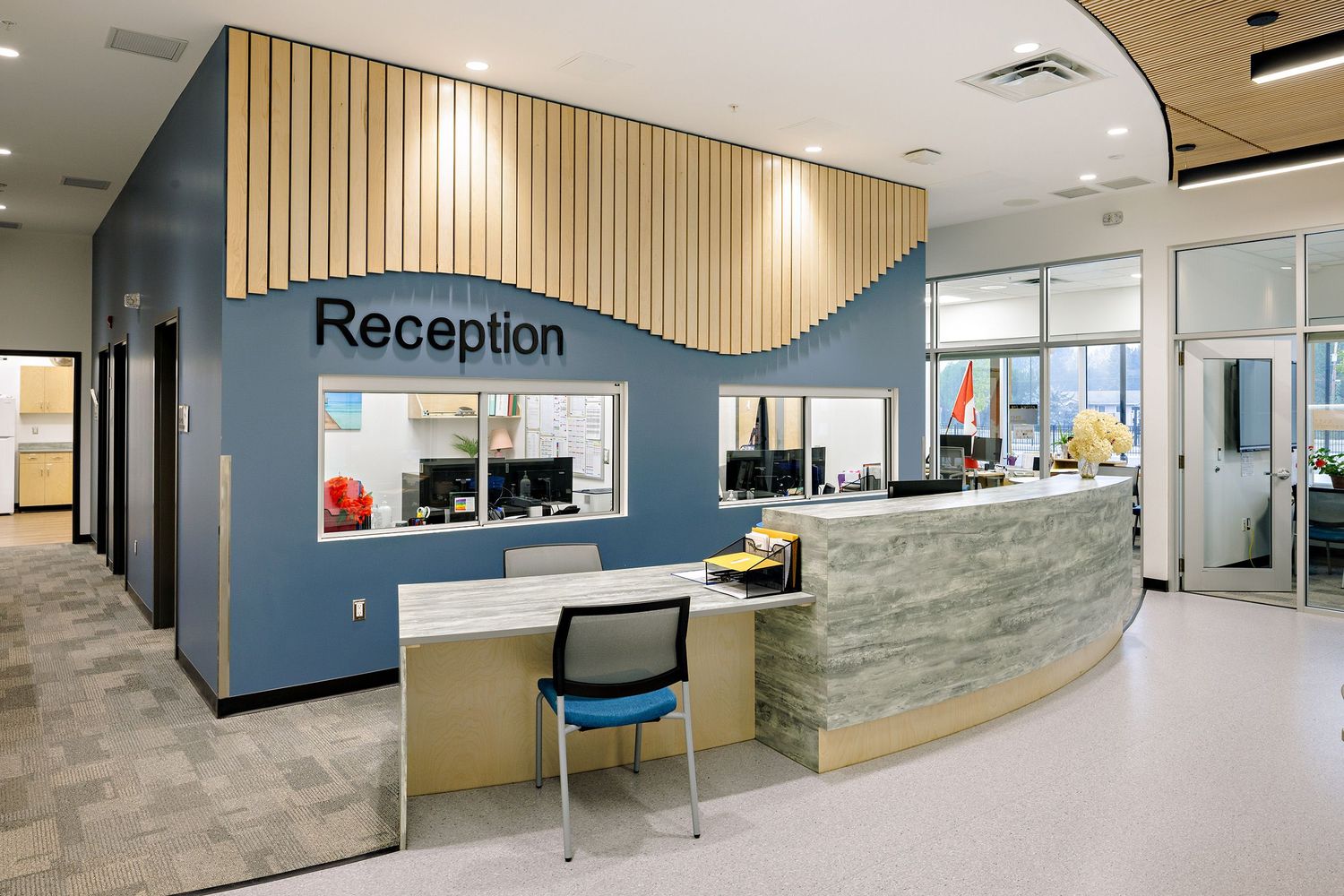 Modern office reception area featuring a curved desk with blue walls and vertical wooden slat accent panels.