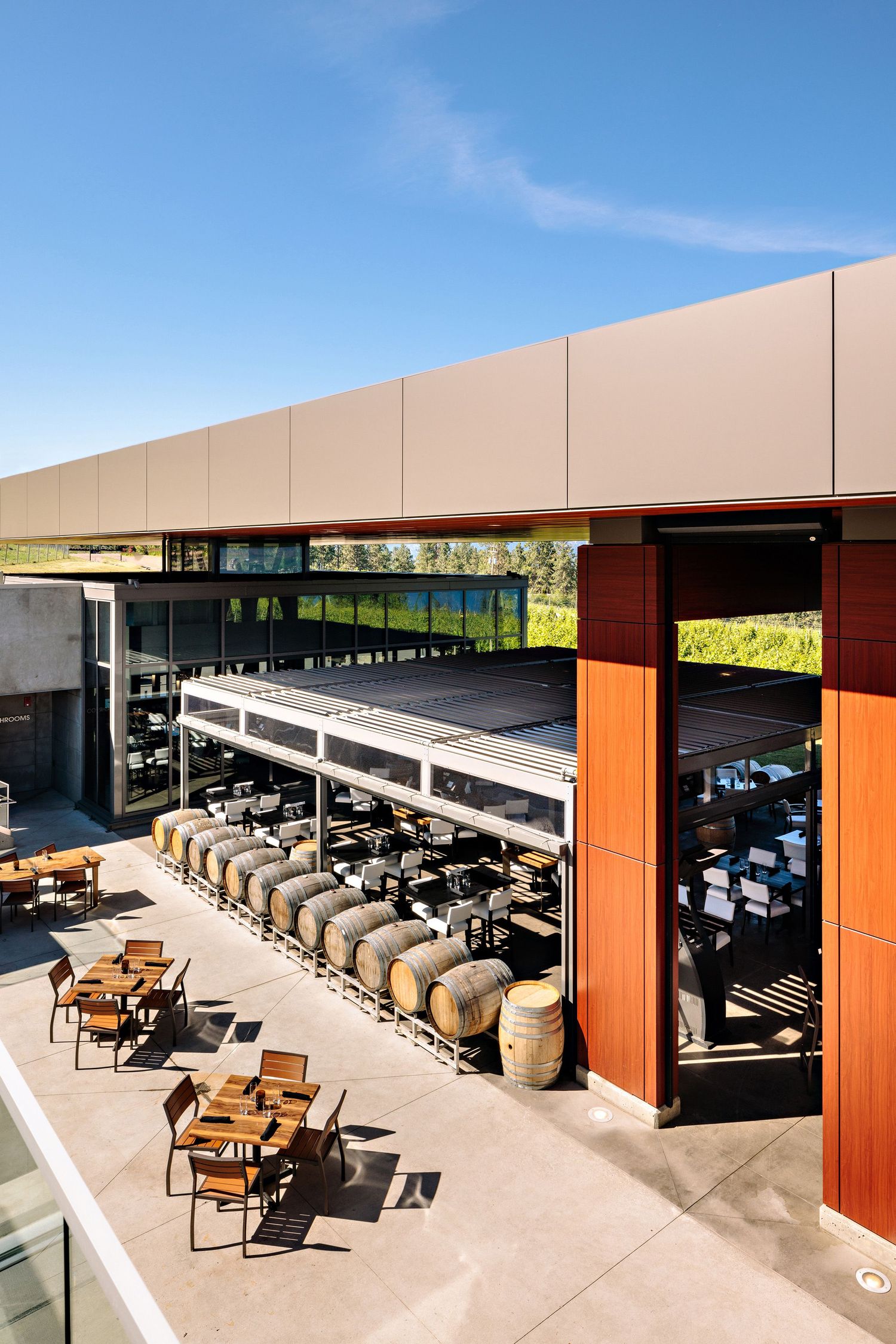 Modern outdoor patio seating area with wooden chairs and tables under a covered terrace at an upscale restaurant or winery.
