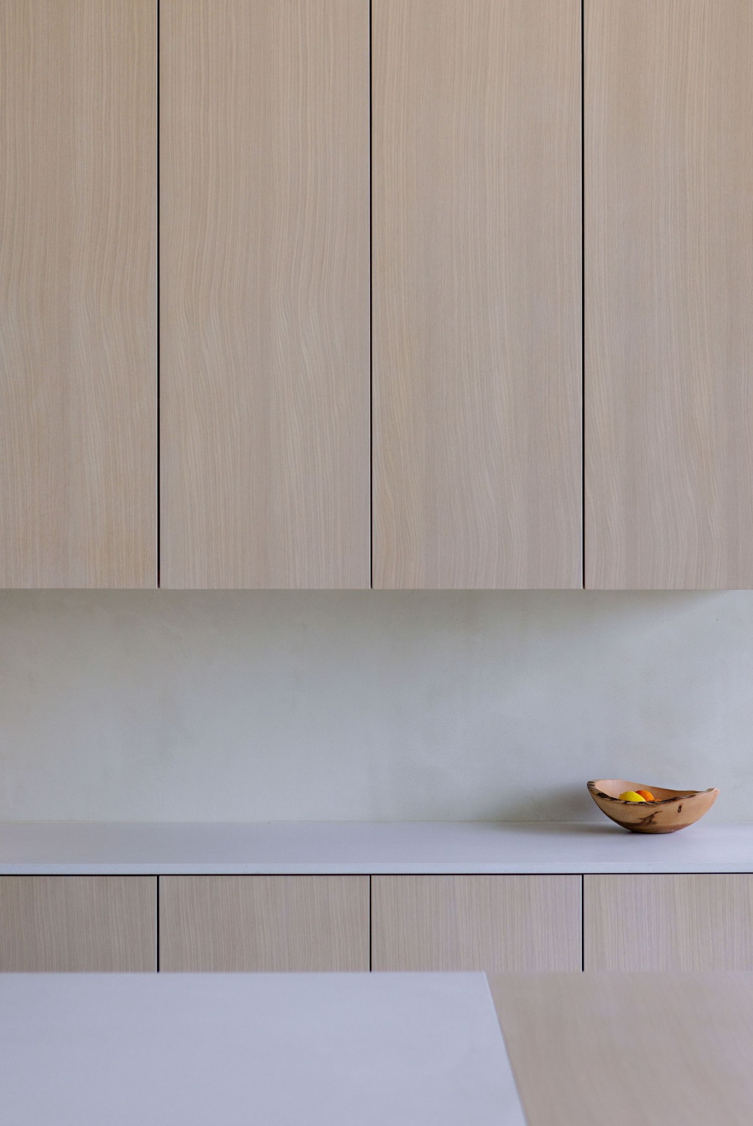 Minimalist interior design featuring light wood cabinets and white counter with small decorative bowl.