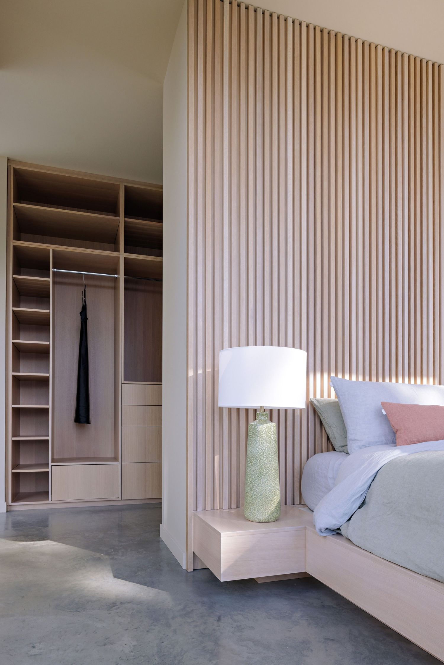 Modern bedroom interior with wooden slat wall accent, built-in closet storage, and sage green ceramic table lamp.