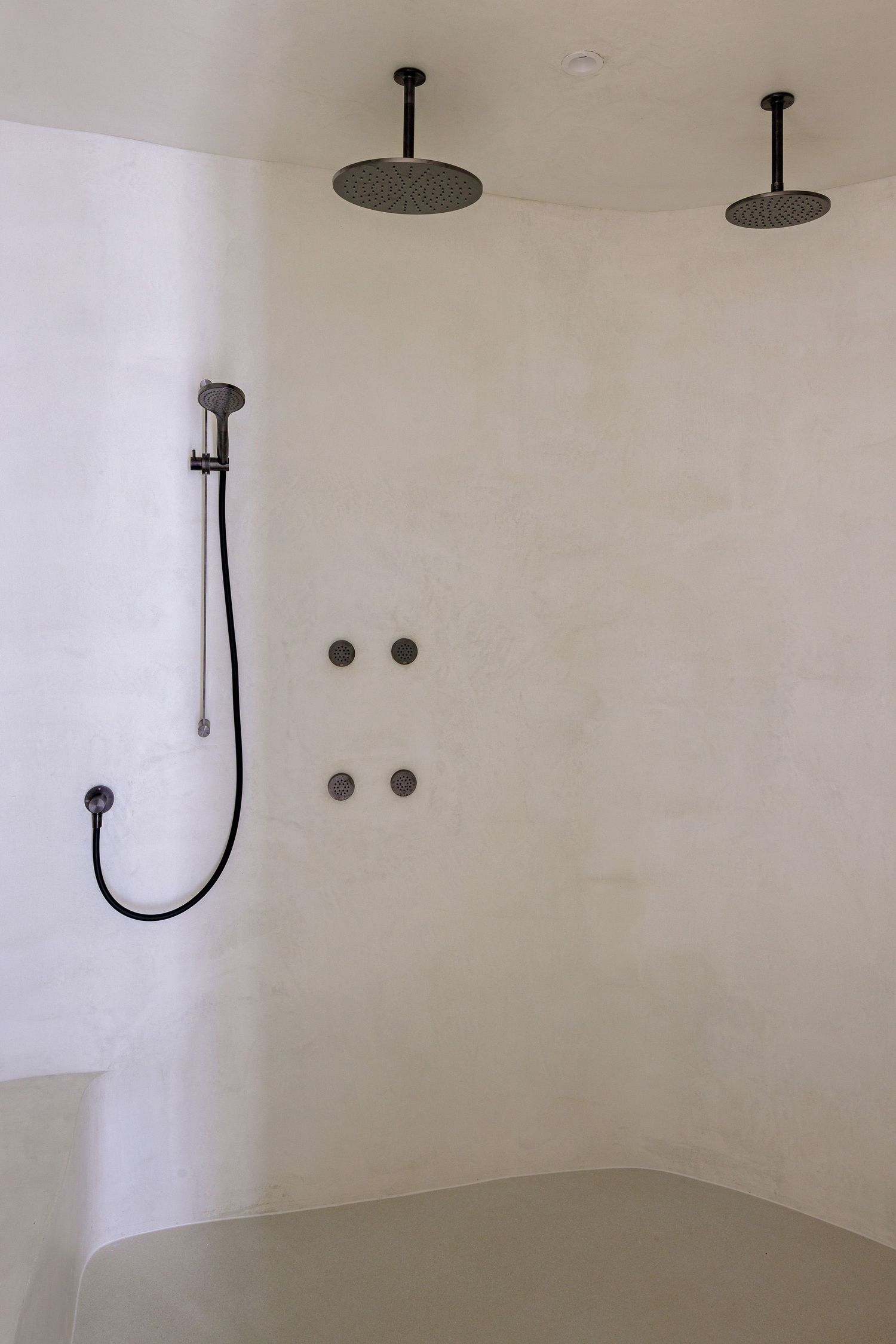 Minimalist shower space with dual ceiling-mounted rain showerheads and curved white walls.