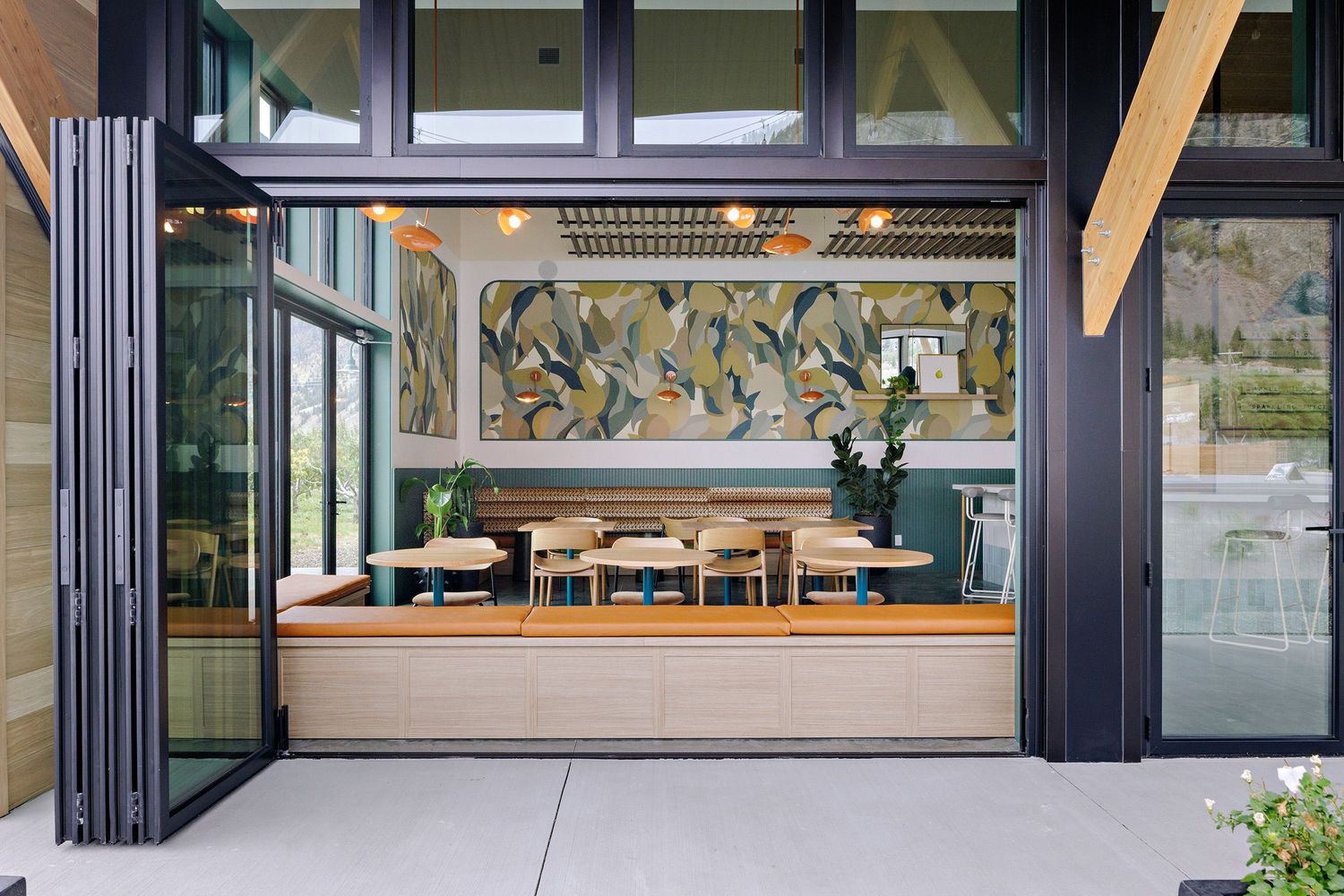 Modern restaurant storefront with folding glass doors and wooden banquette seating beneath decorative wall art.