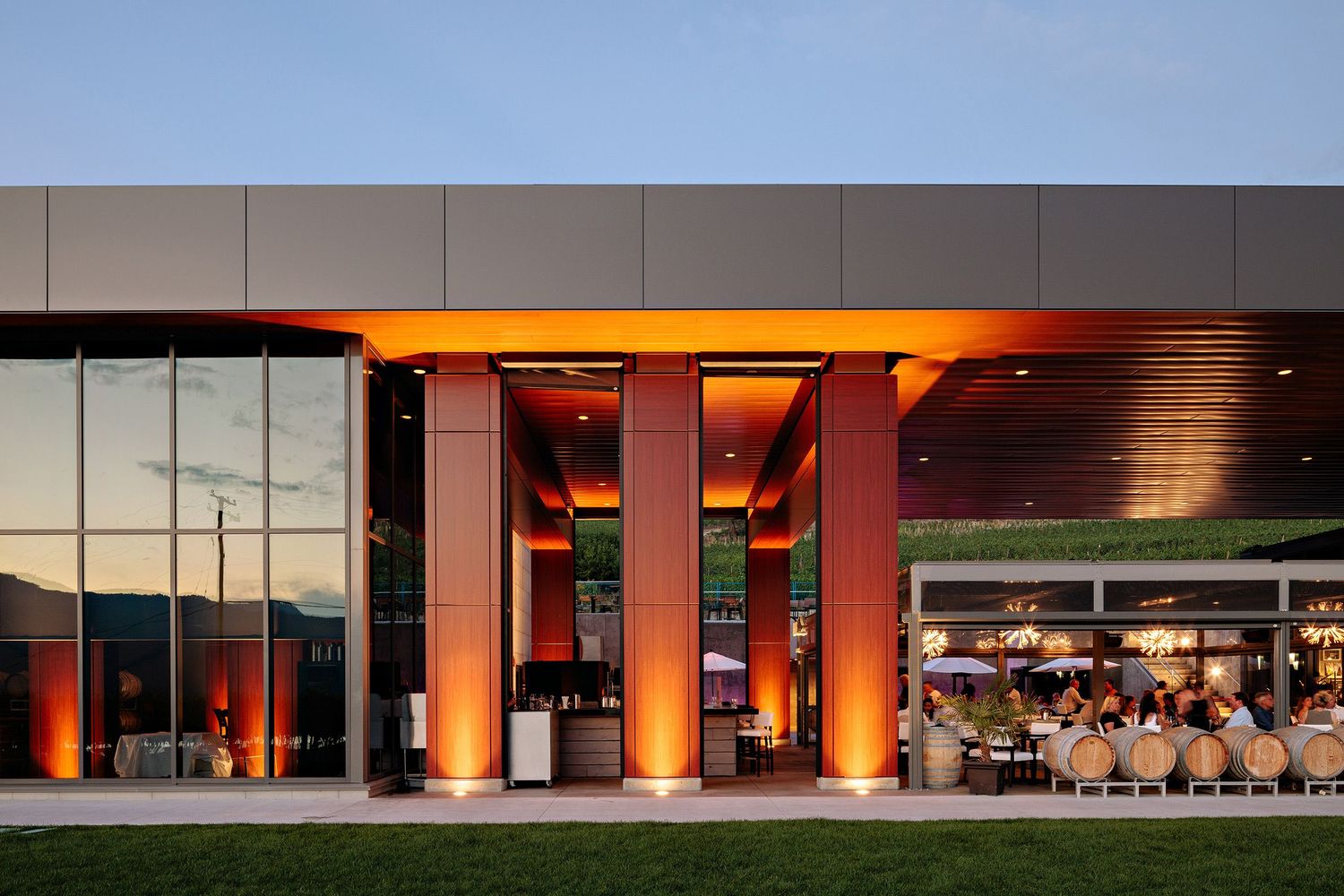 Modern restaurant exterior with orange illuminated pillars and outdoor patio seating at sunset.