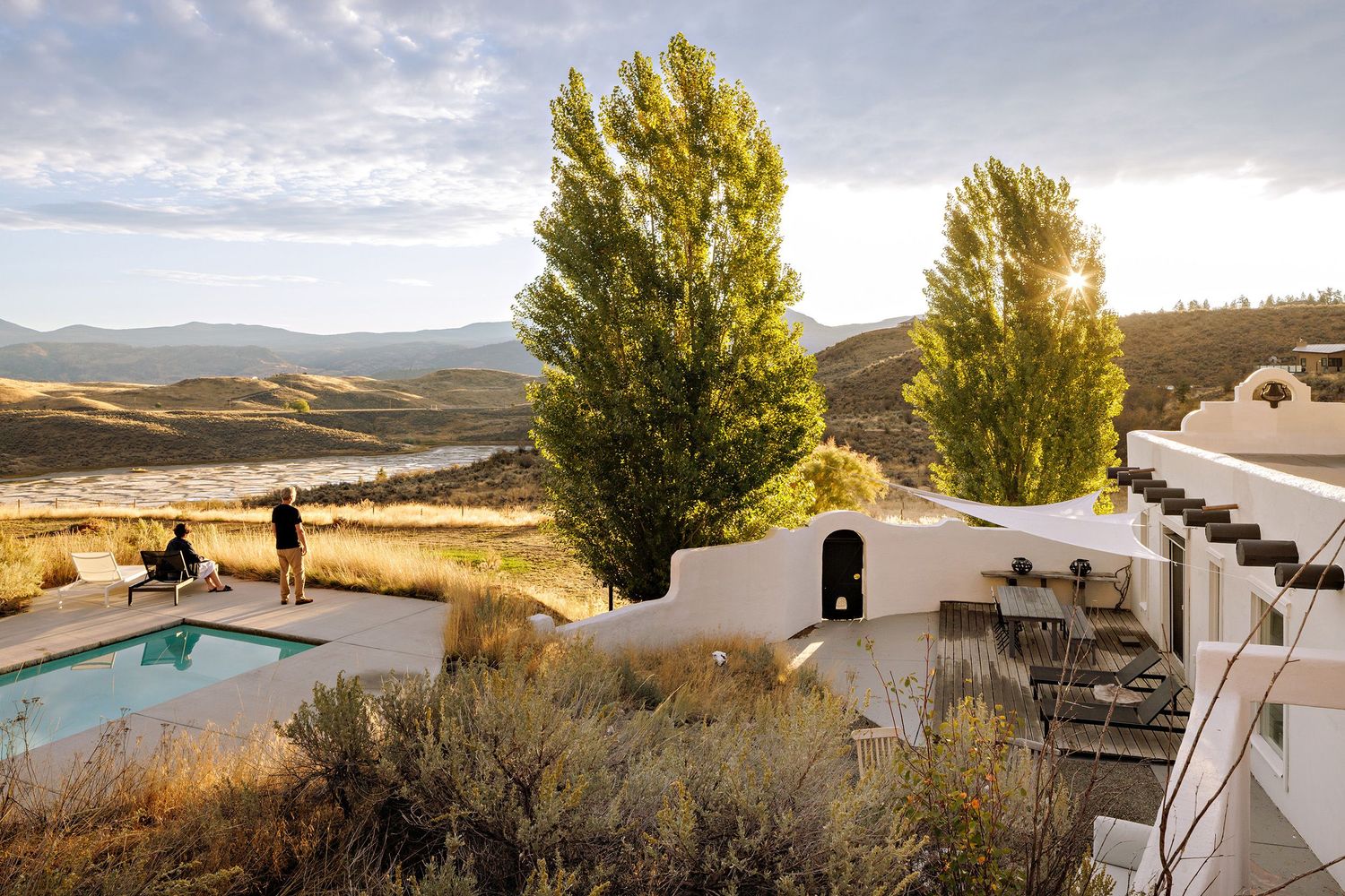 Luxury resort pool overlooking rolling hills with tall poplar trees and white adobe buildings at sunrise.