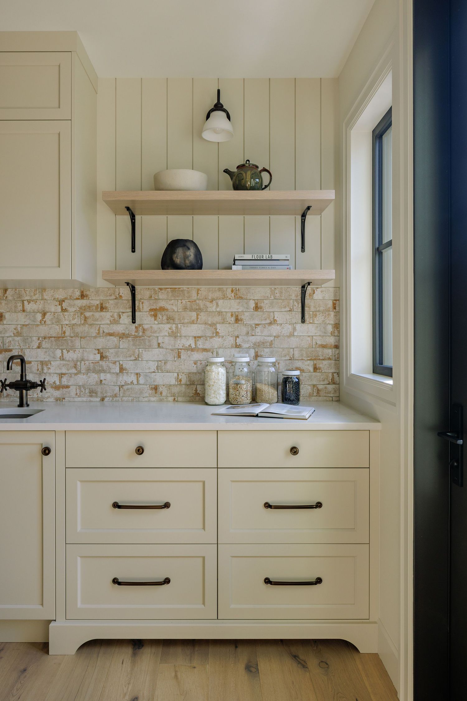 Cream colored kitchen cabinets with stone backsplash and dark hardware create a modern farmhouse look.