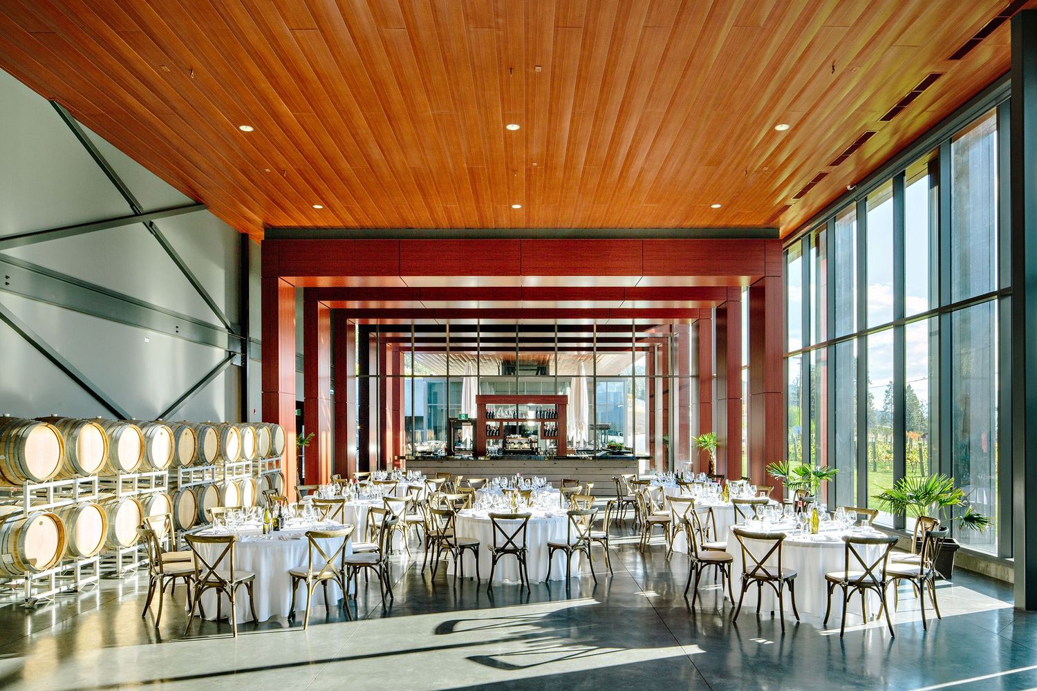 Modern restaurant dining room with wood ceiling, floor-to-ceiling windows, and white tables and chairs.