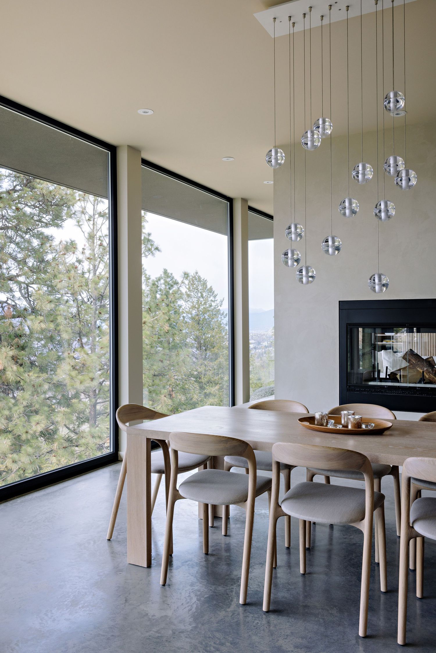 Modern dining room with floor-to-ceiling windows, wooden table, minimalist chairs and cascading glass pendant lights.