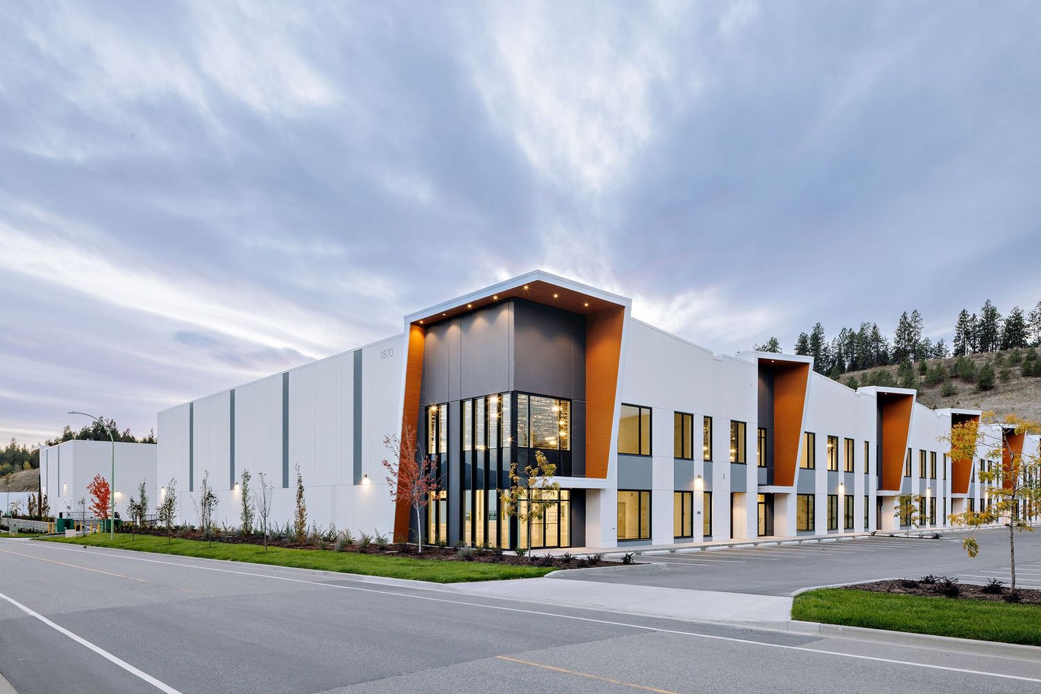 Contemporary industrial building with orange accents and floor-to-ceiling windows along a pristine landscaped street.