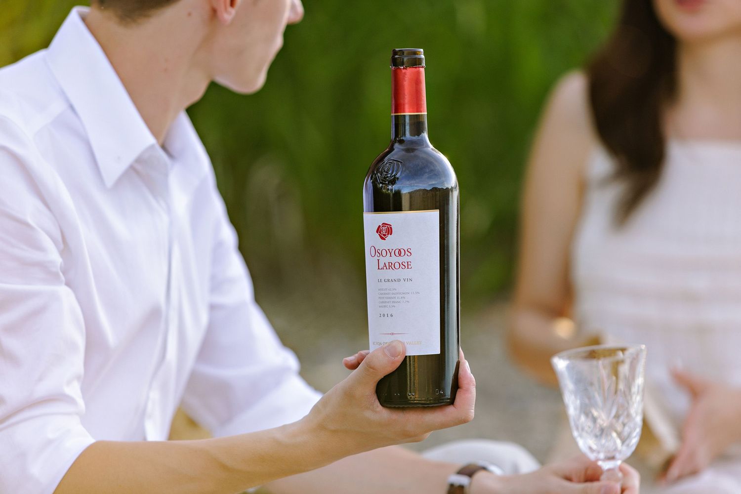 A bottle of red wine being presented at an outdoor dining table with wine glasses.