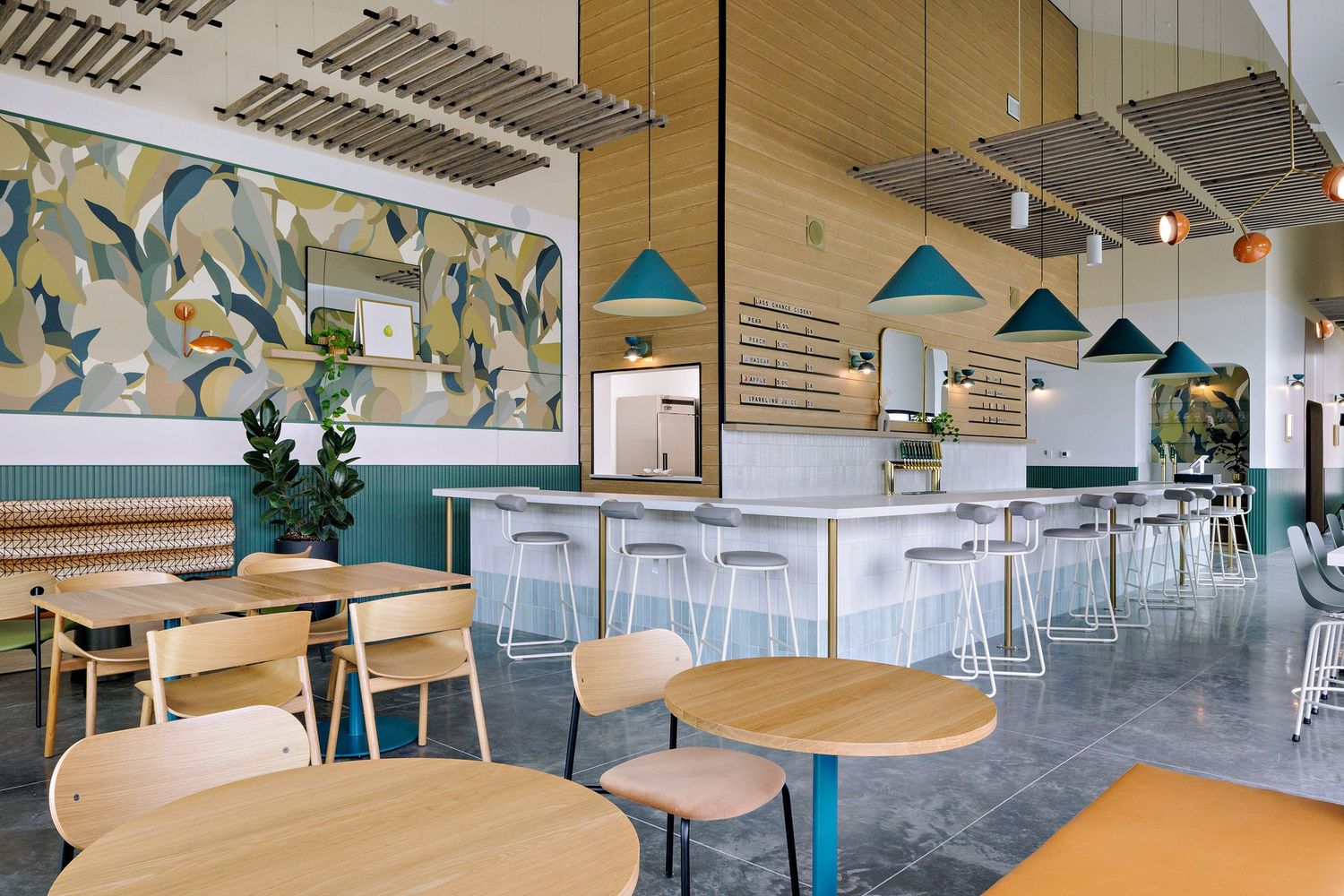 Bright restaurant space with teal accents, pendant lights, and round dining tables on concrete floors.