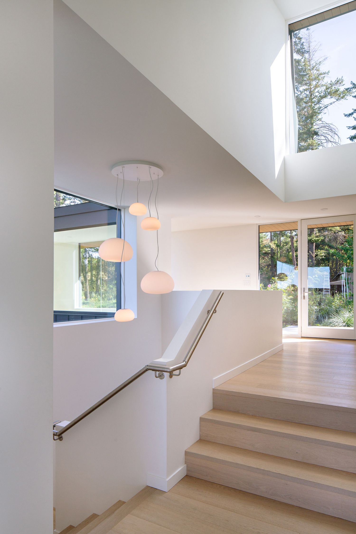 Modern staircase with wooden steps and handrail features unique cloud-like pendant lights and tall windows letting in natural light.