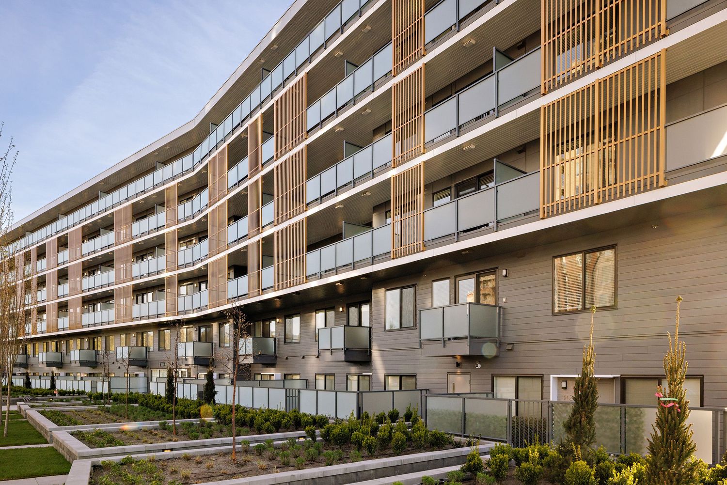 Modern apartment building exterior with curved facade, wooden accents, and landscaped grounds at dusk.