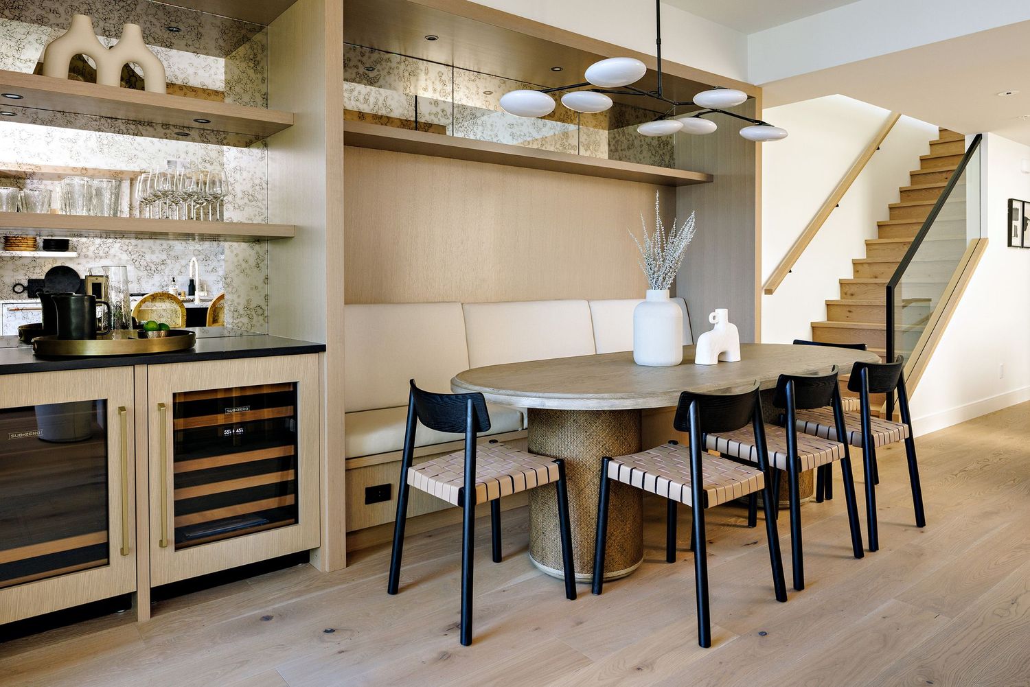 Dining area with black chairs and built-in wine storage under wooden stairs.