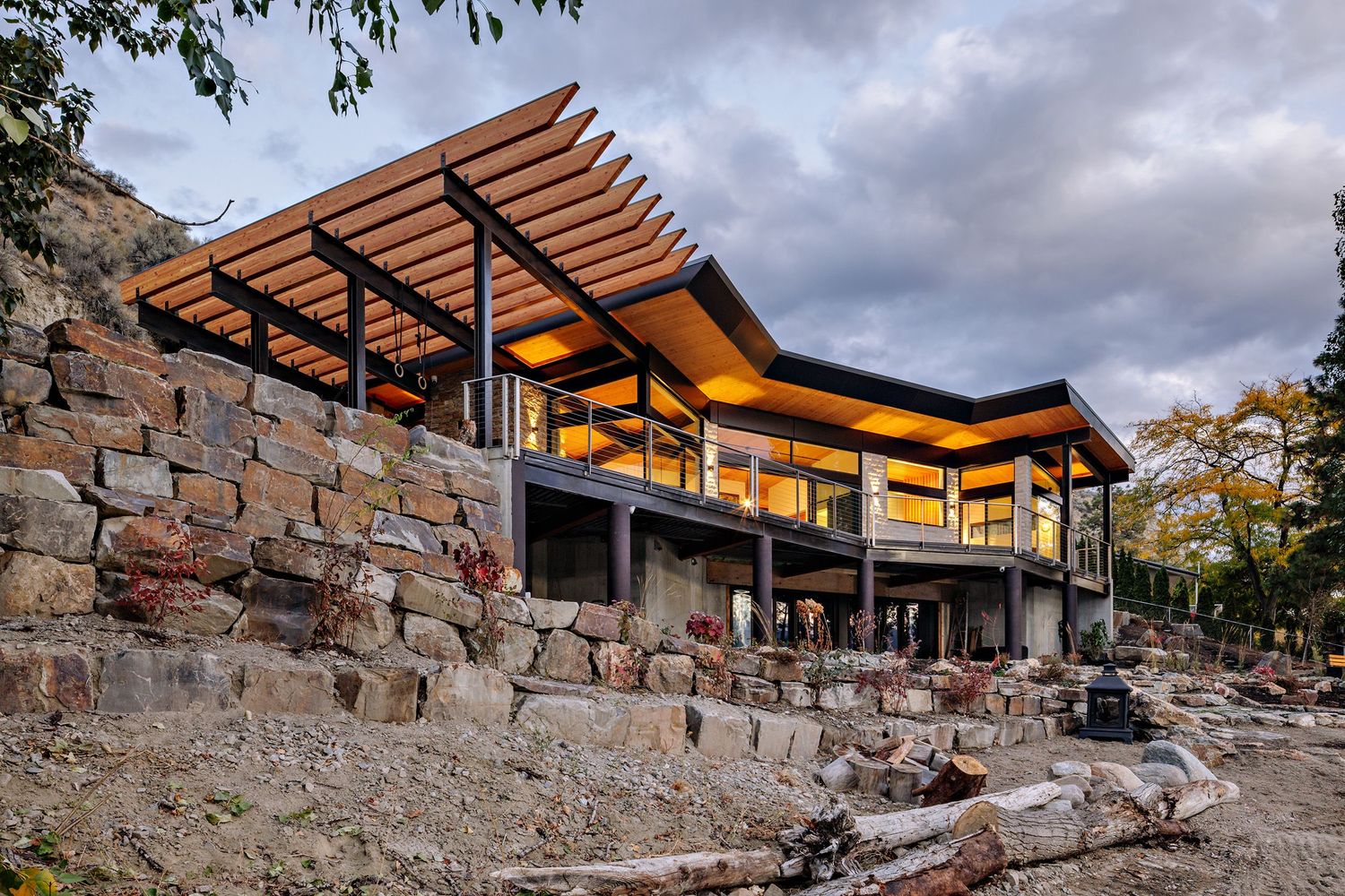 Modern hillside home with stone retaining walls and wood-slatted overhangs showcases dramatic architectural design.