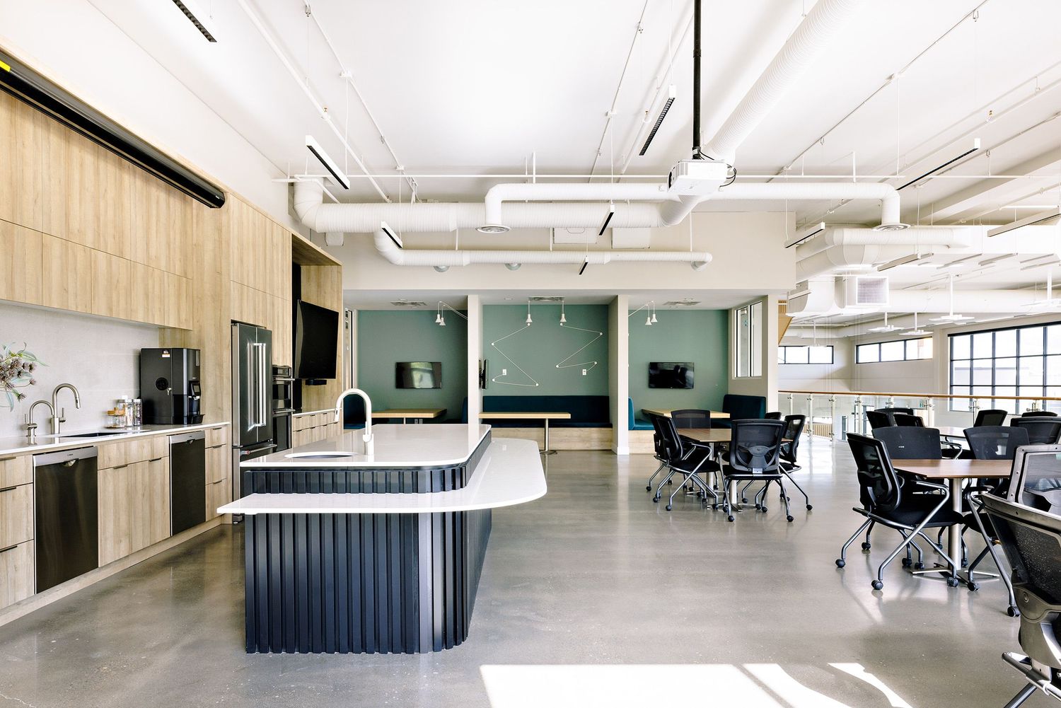 Modern open office space with green accent walls, light wood cabinetry, and collaborative workstations arranged throughout.