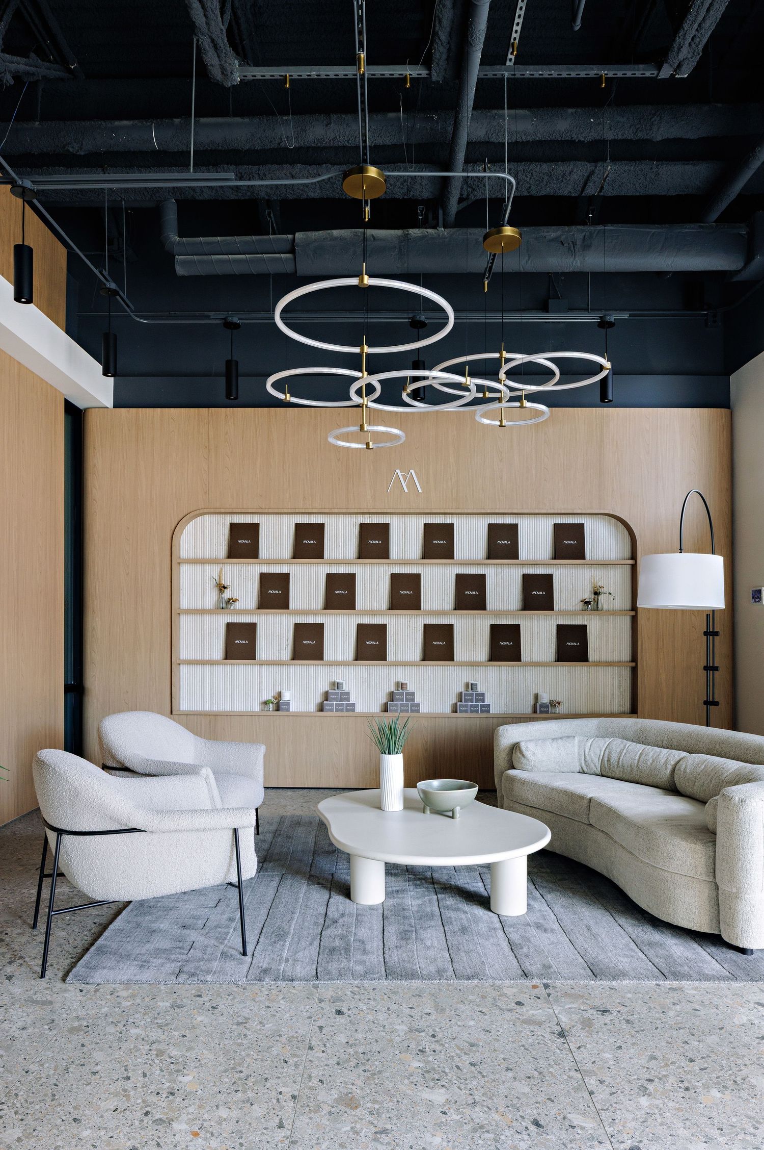 Modern lounge area with circular pendant lights, curved sofa, accent chair and built-in wall shelving against beige walls.