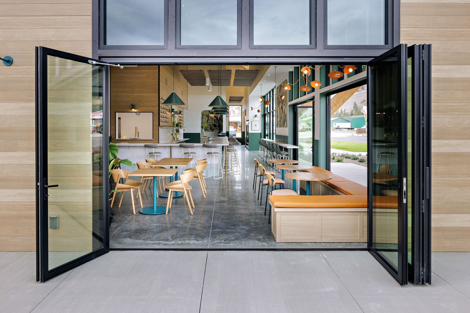 Modern cafe interior with glass doors, wooden accents, and concrete floors showing seating area and natural lighting.