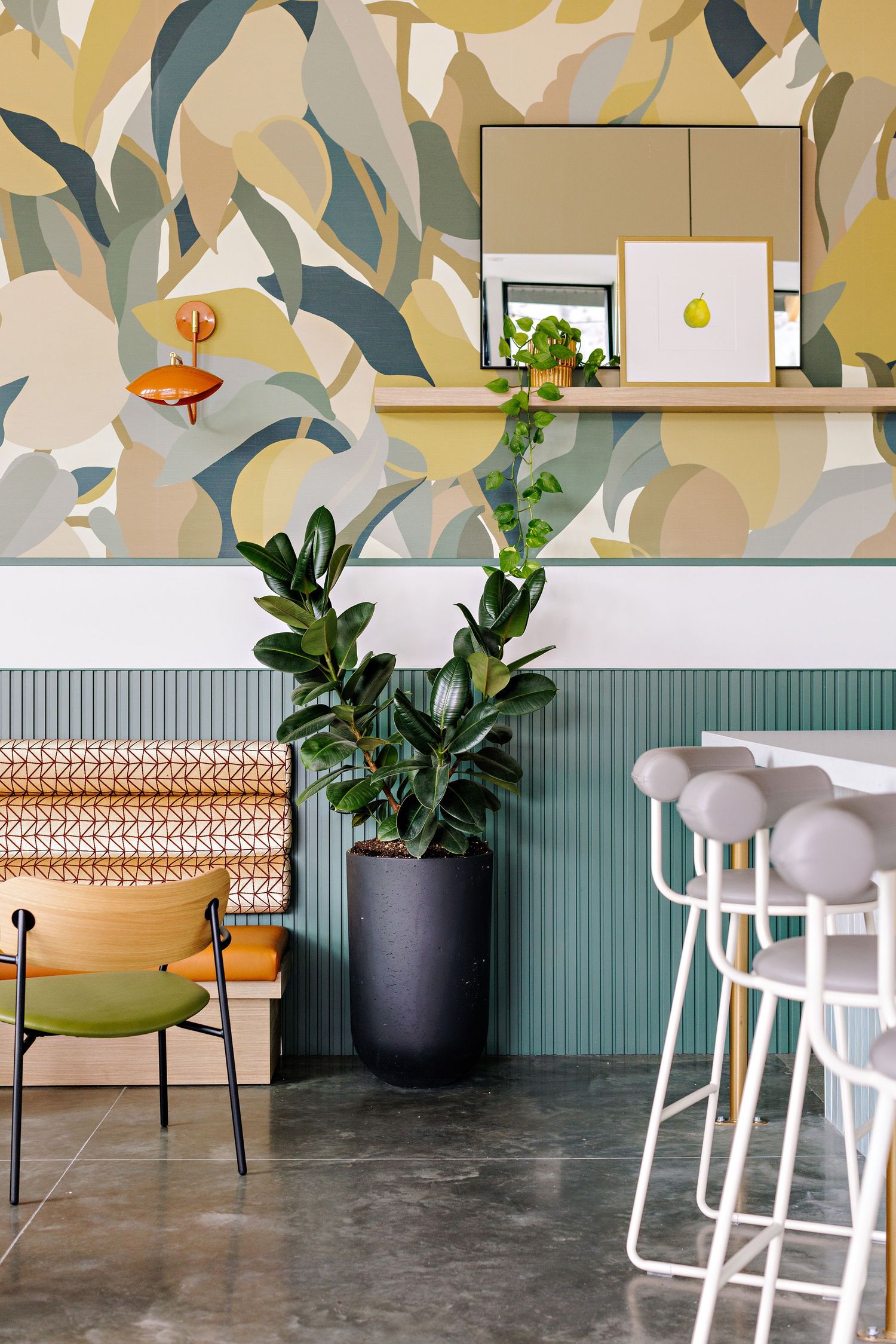 Modern restaurant interior with green potted plant, stylish seating, and abstract wallpaper against sage wainscoting.
