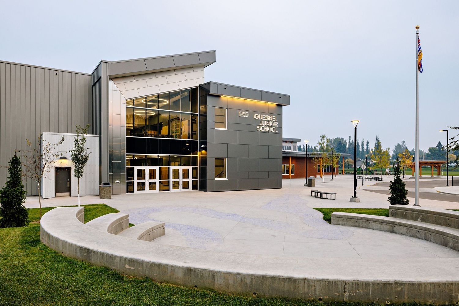 Modern gray and glass community center building with curved concrete plaza and flag pole outside.