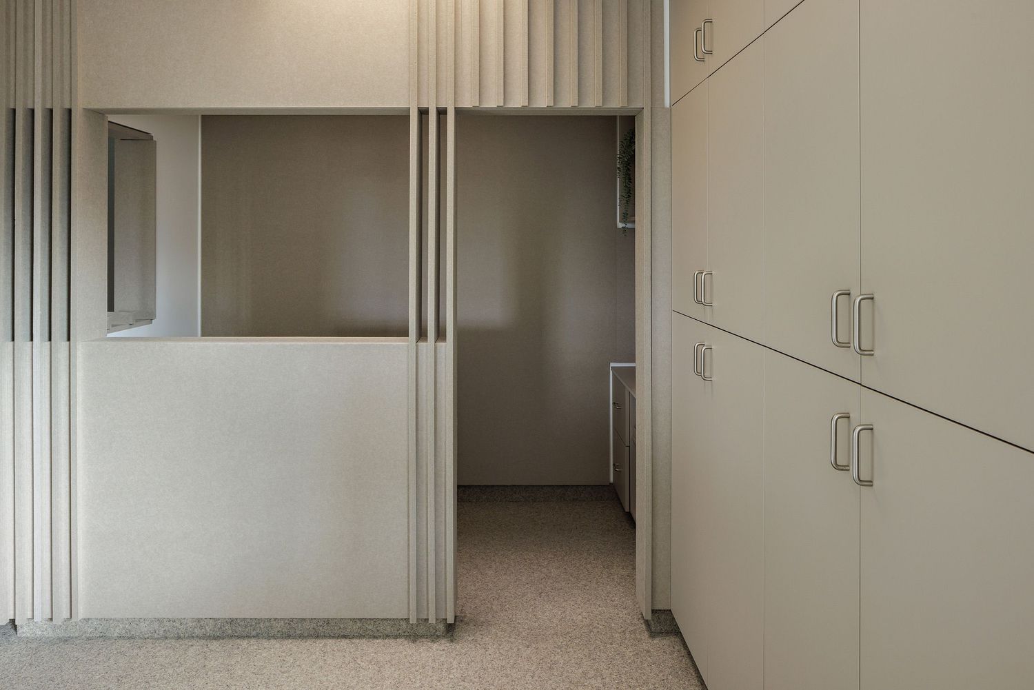 Interior hallway with beige walls, built-in storage cabinets, and vertical architectural details leading to a doorway.