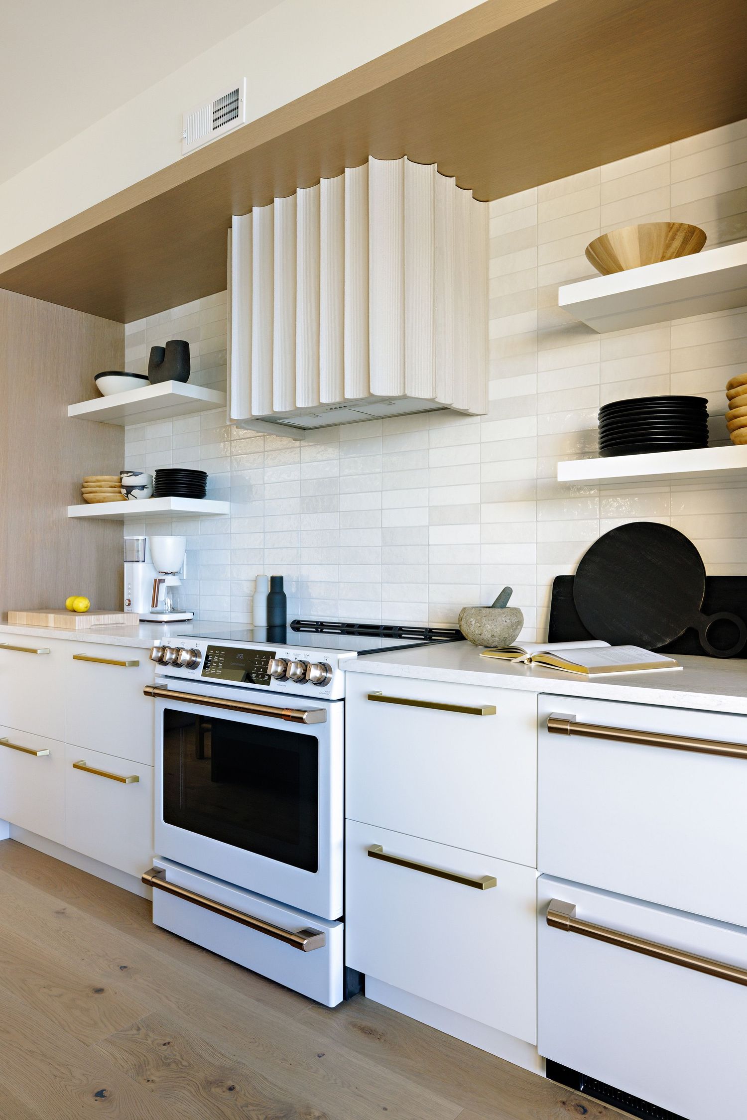 White kitchen with modern range hood, floating shelves, and brass hardware details.