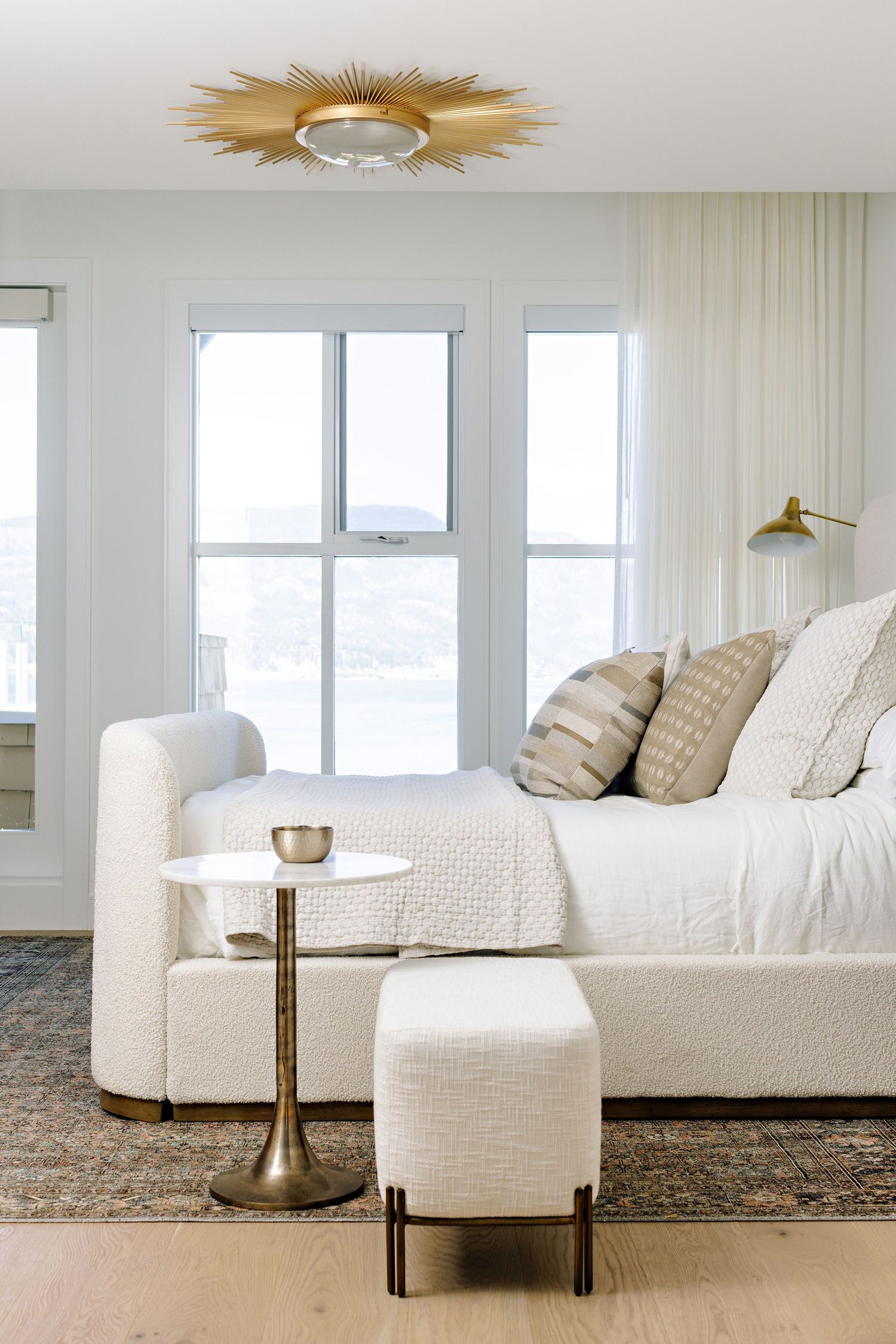 Bright living space with white upholstered chaise, gold sunburst ceiling light, and large windows.