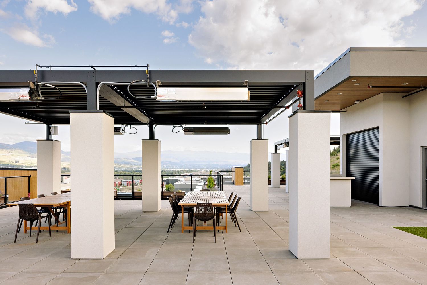 Rooftop terrace dining area with white columns and pergola offering outdoor workspace views.