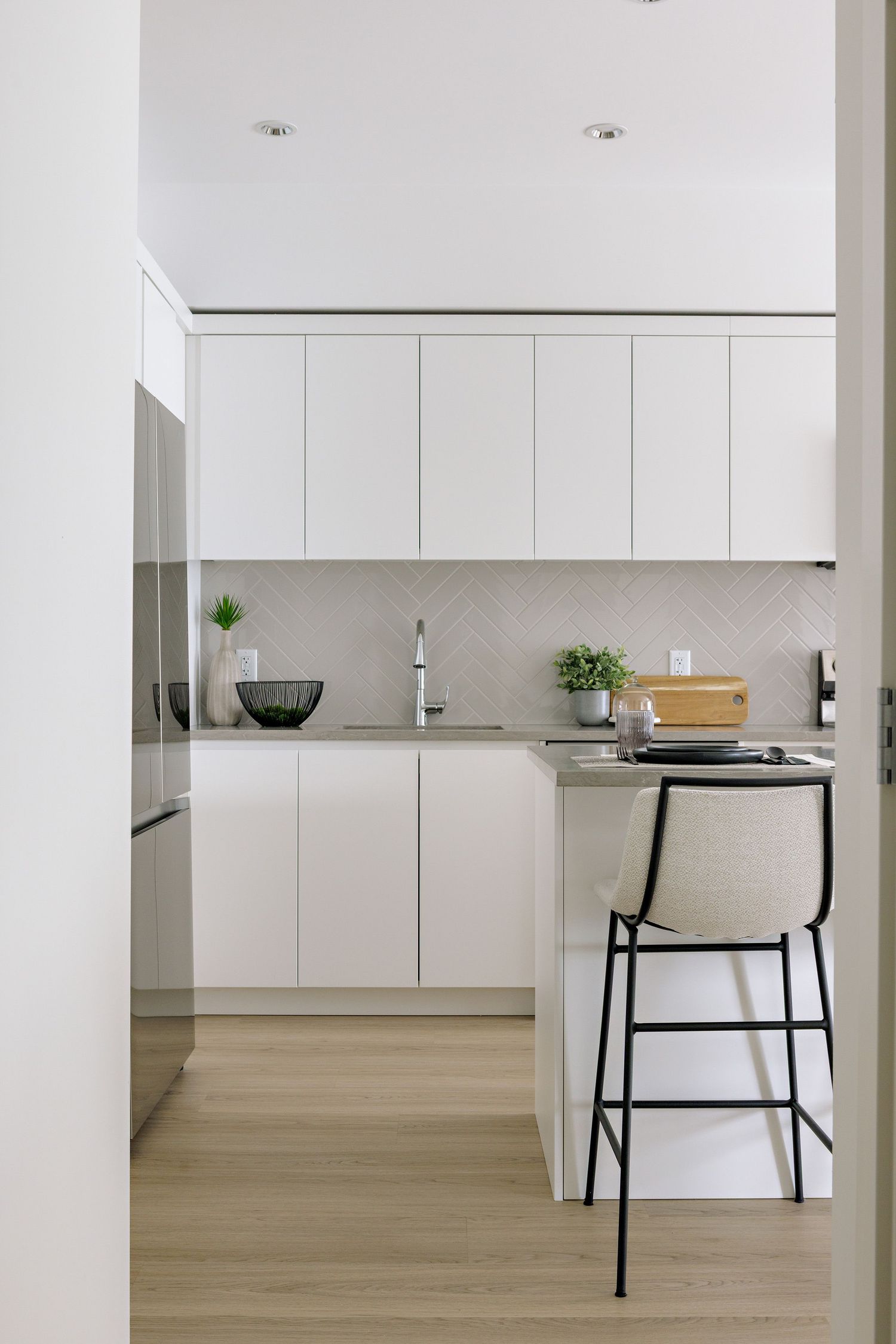 Modern minimalist white kitchen with marble backsplash, sleek cabinets and a tall bar stool in a clean design style.