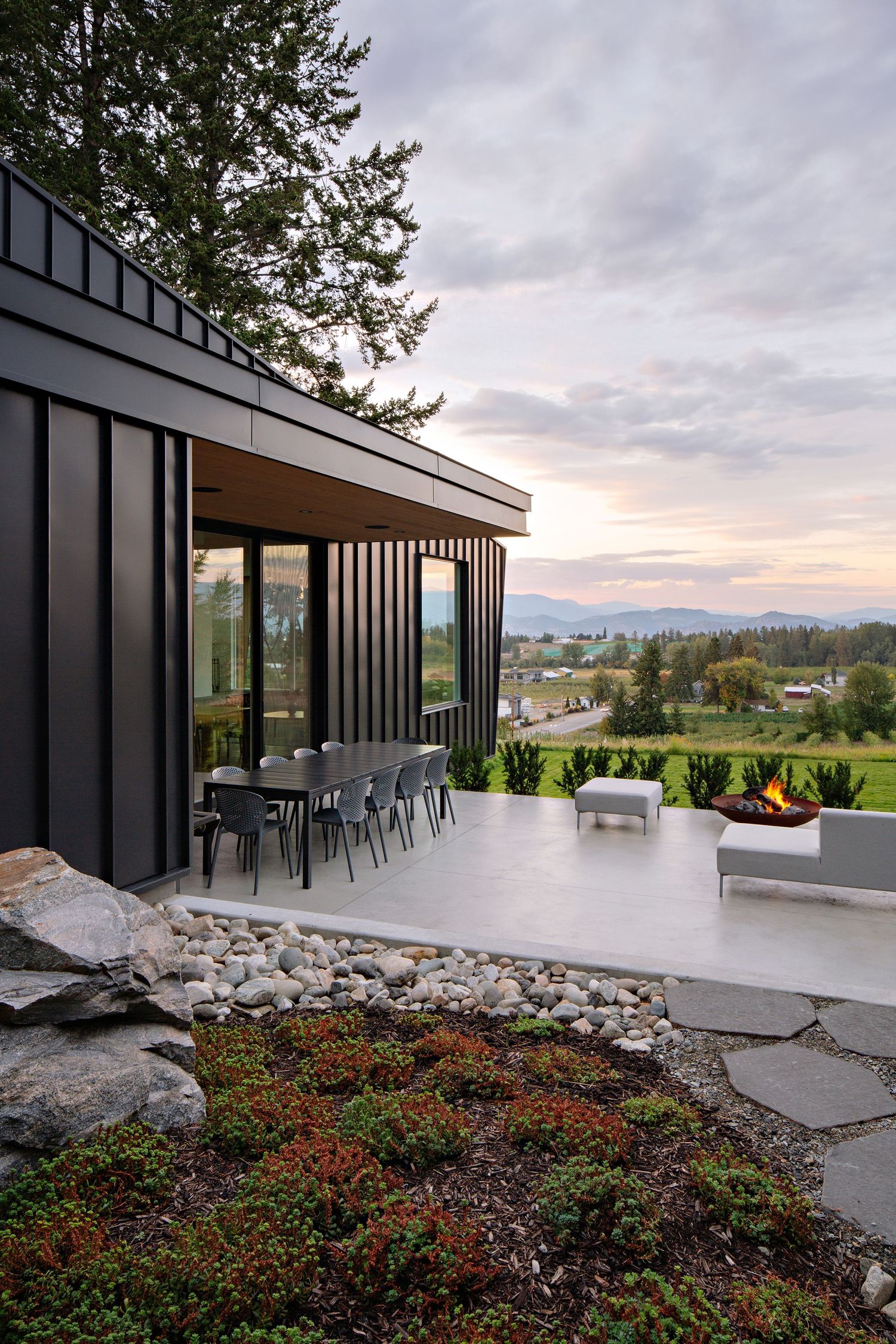 Modern mountain home with covered patio featuring outdoor seating, fire pit and scenic valley views at sunset.