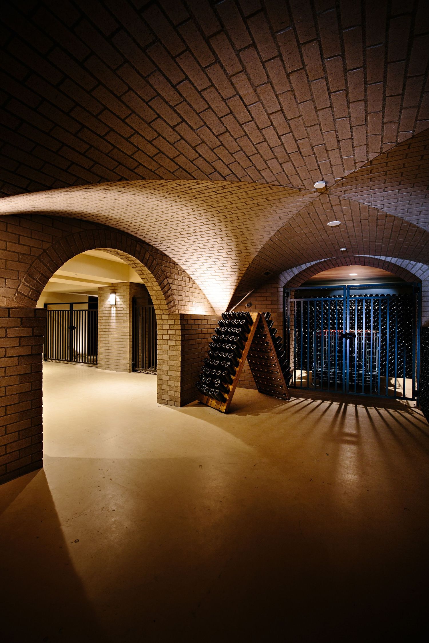 Illuminated brick wine cellar with curved vaulted ceiling and arched passageways in warm lighting.
