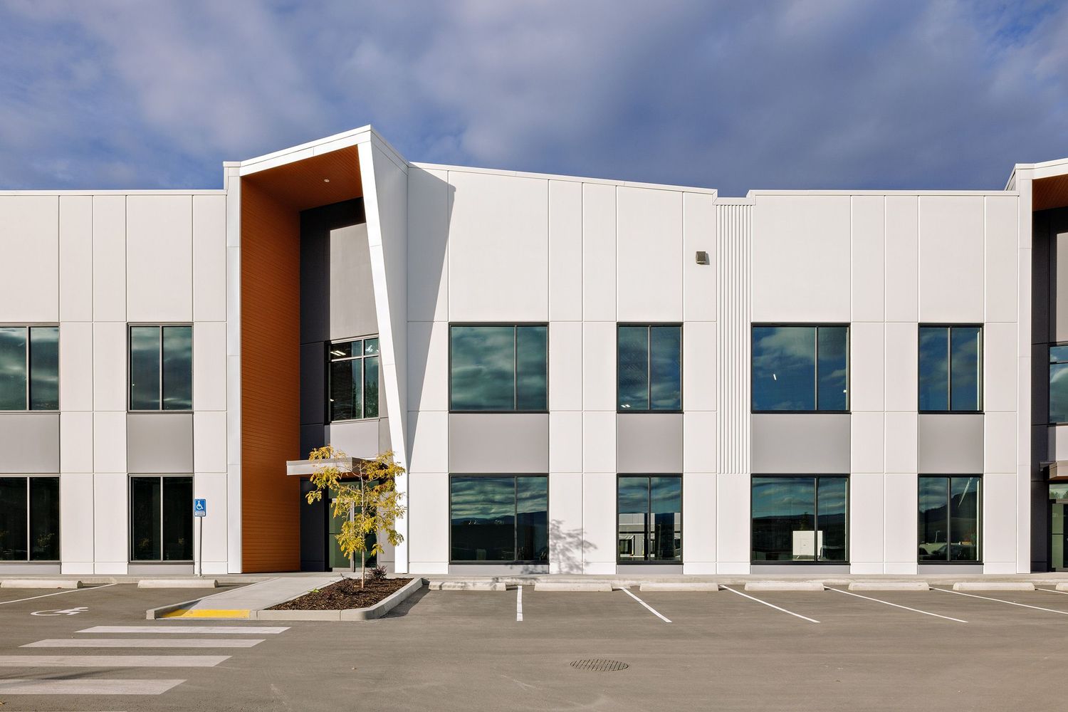 Modern white commercial office building exterior with angular entrance design and glass windows in business park setting.