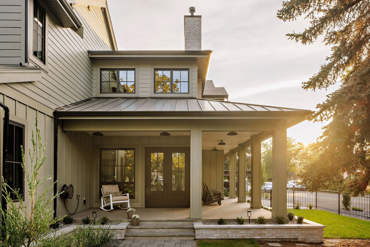 Modern farmhouse exterior features white siding, black trim, and large windows illuminated by warm sunset light.